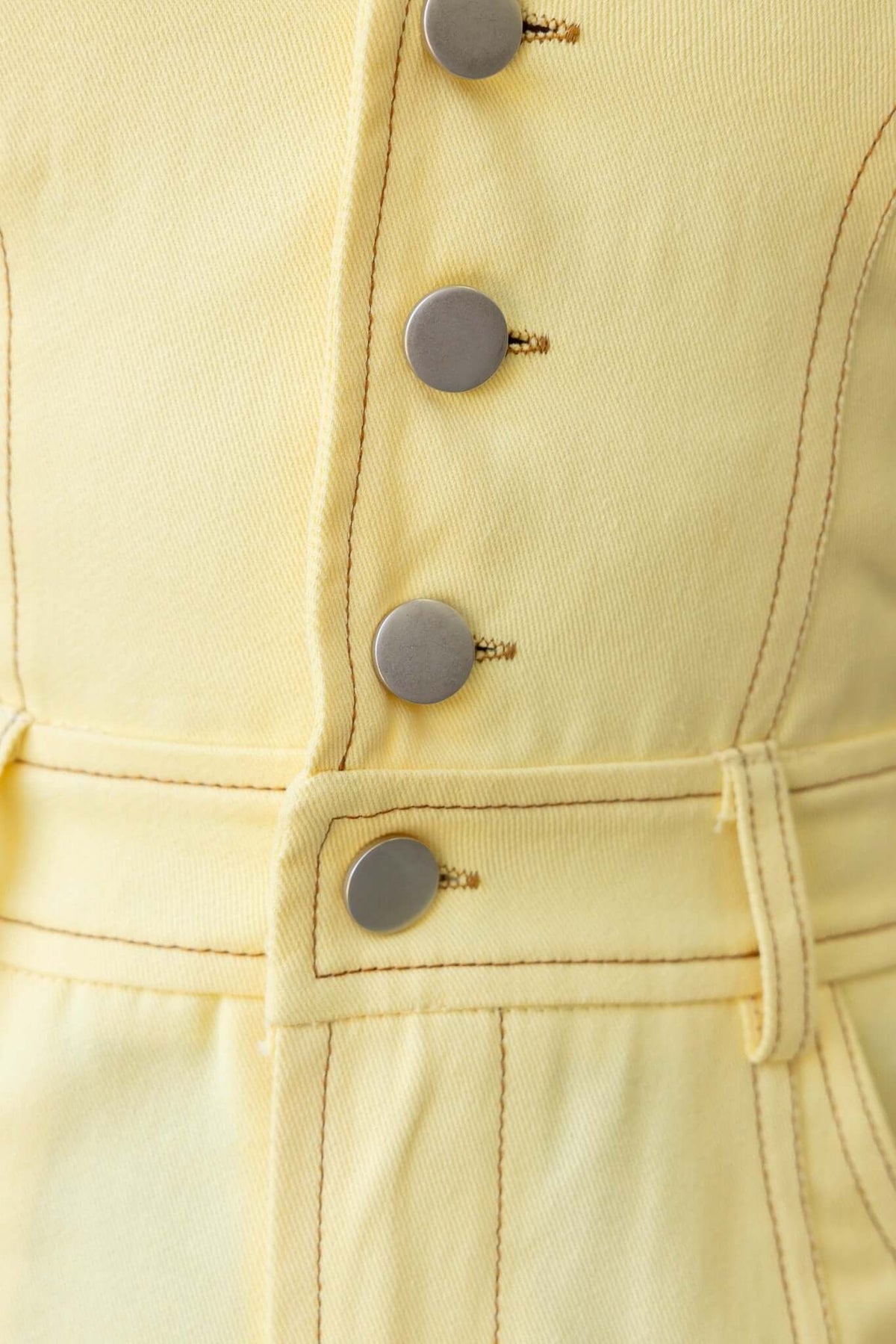Close-up of yellow denim playsuit with button-up detail and stylish stitching.