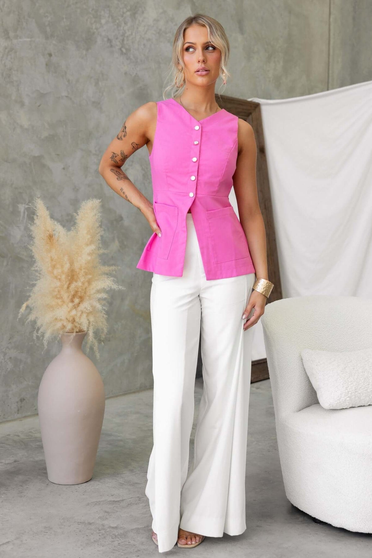 Fashion model wearing a pink vest top with button-up front and white wide-leg pants, styled in a chic indoor setting.