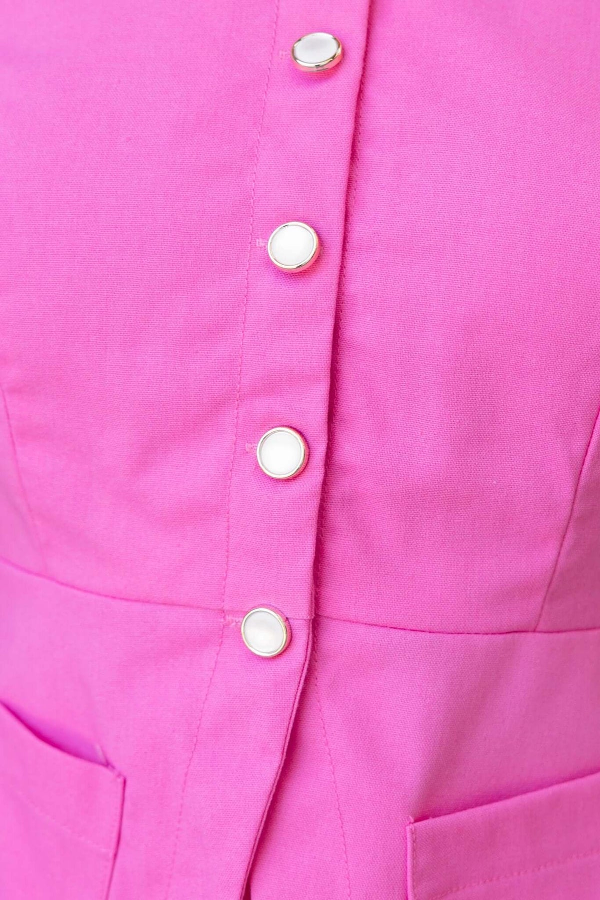 Close-up of a pink vest top featuring a V-neckline, button-up front, and front pockets, showcasing a linen-like texture.