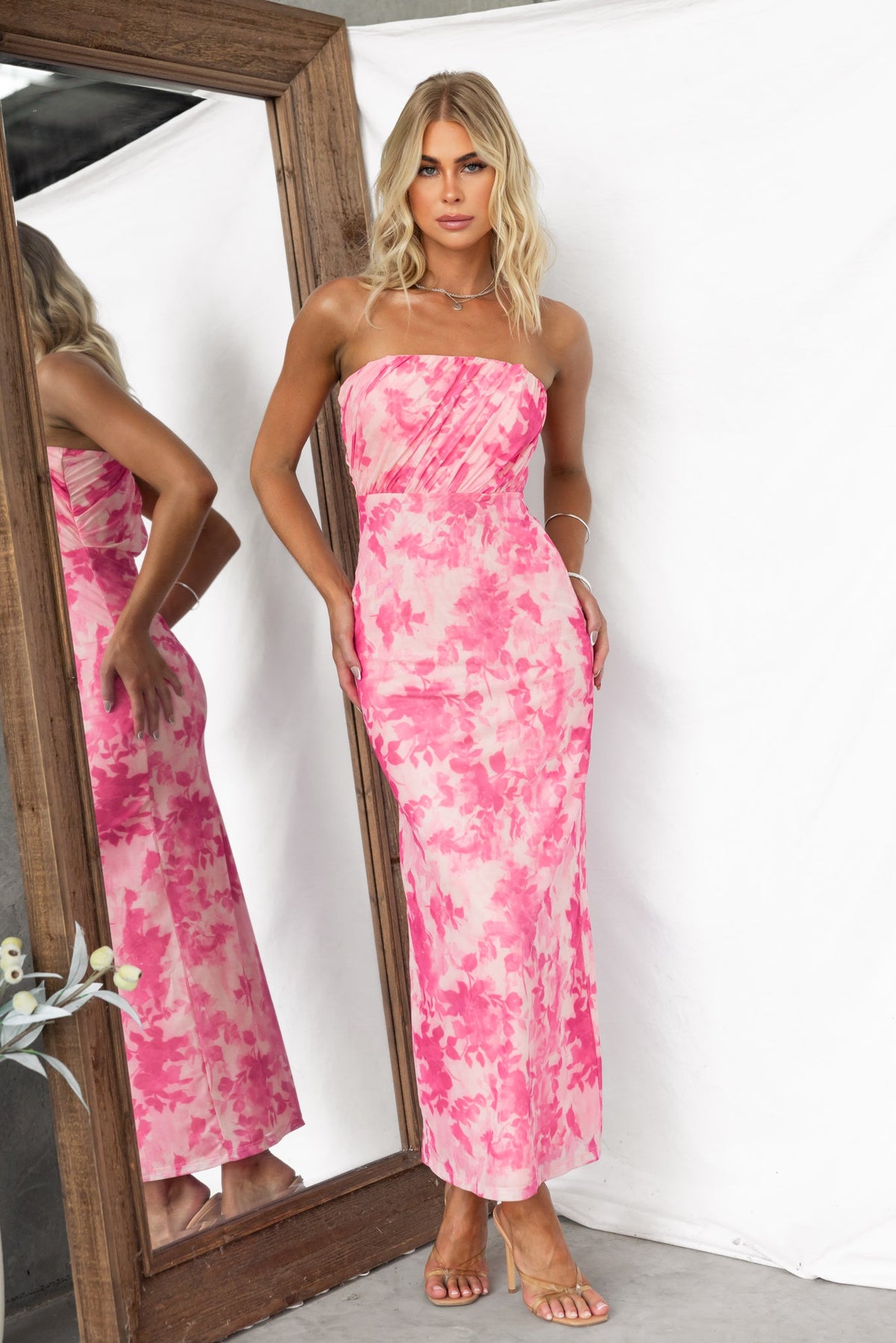 Model wearing a pink floral print strapless maxi dress, showcasing its fitted silhouette and elegant design.