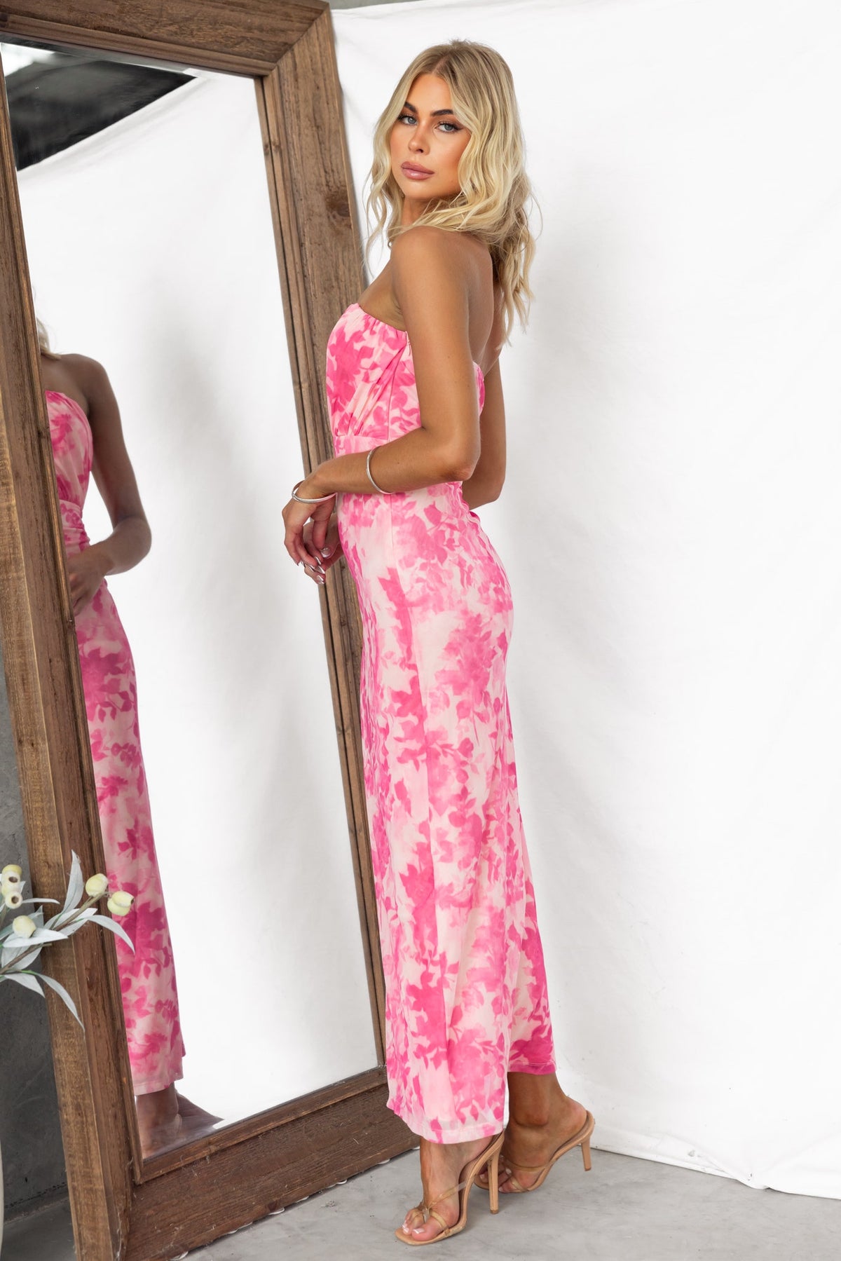 Katia Maxi Dress with floral print, strapless design, and mesh overlay, model wearing pink dress by mirror.