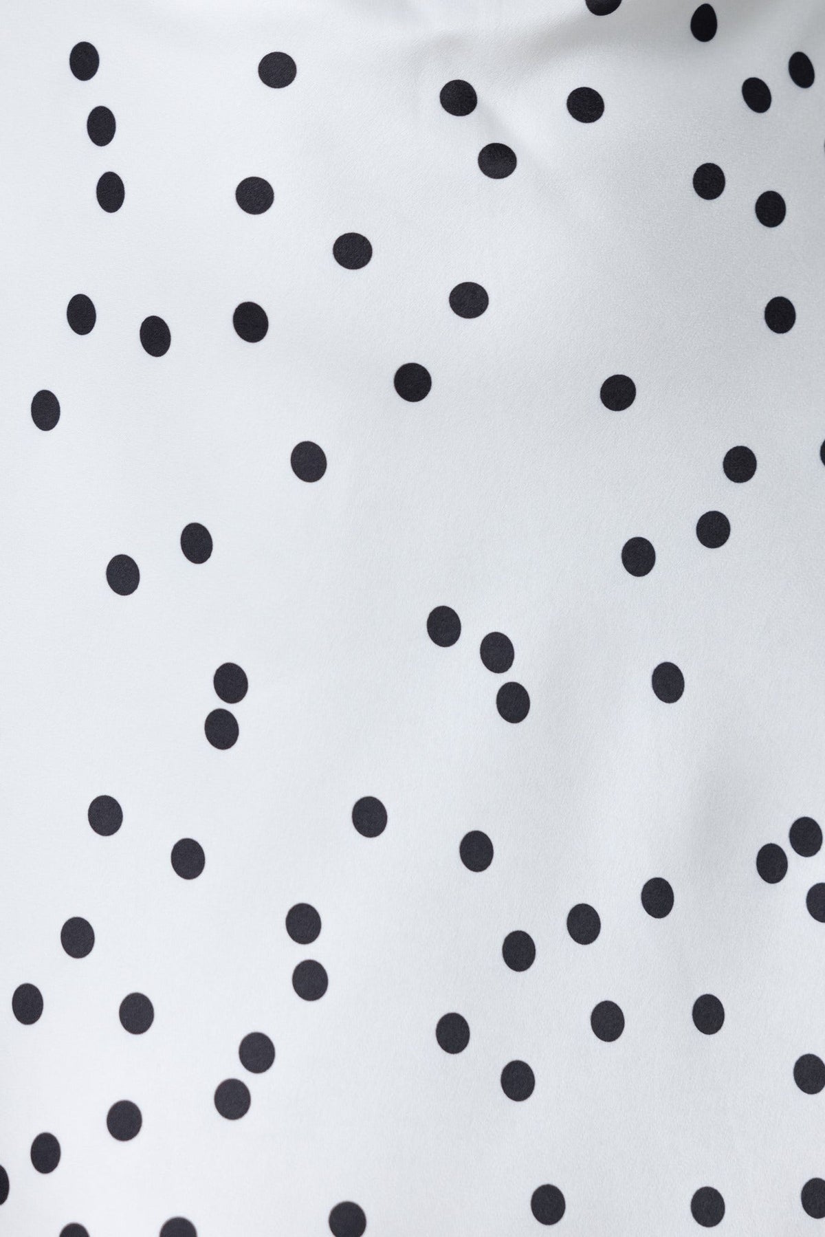 Close-up of the Leary Dress featuring a playful black polka dot print on a white satin fabric.