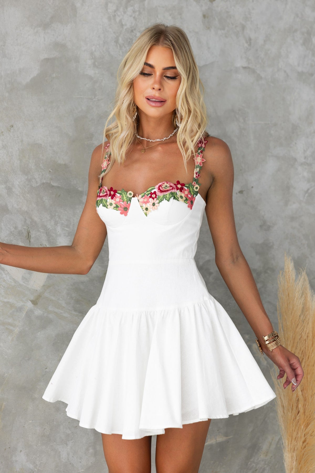 Model wearing the One Last Time Dress with floral embroidery, adjustable straps, and a flared skirt against a textured background.