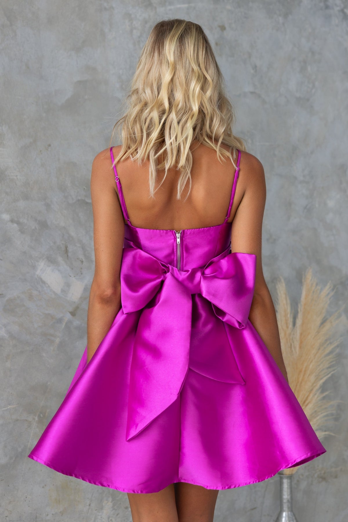 Back view of a rosebud dress in vibrant pink with a large bow and adjustable straps, showcasing a stylish and elegant design.