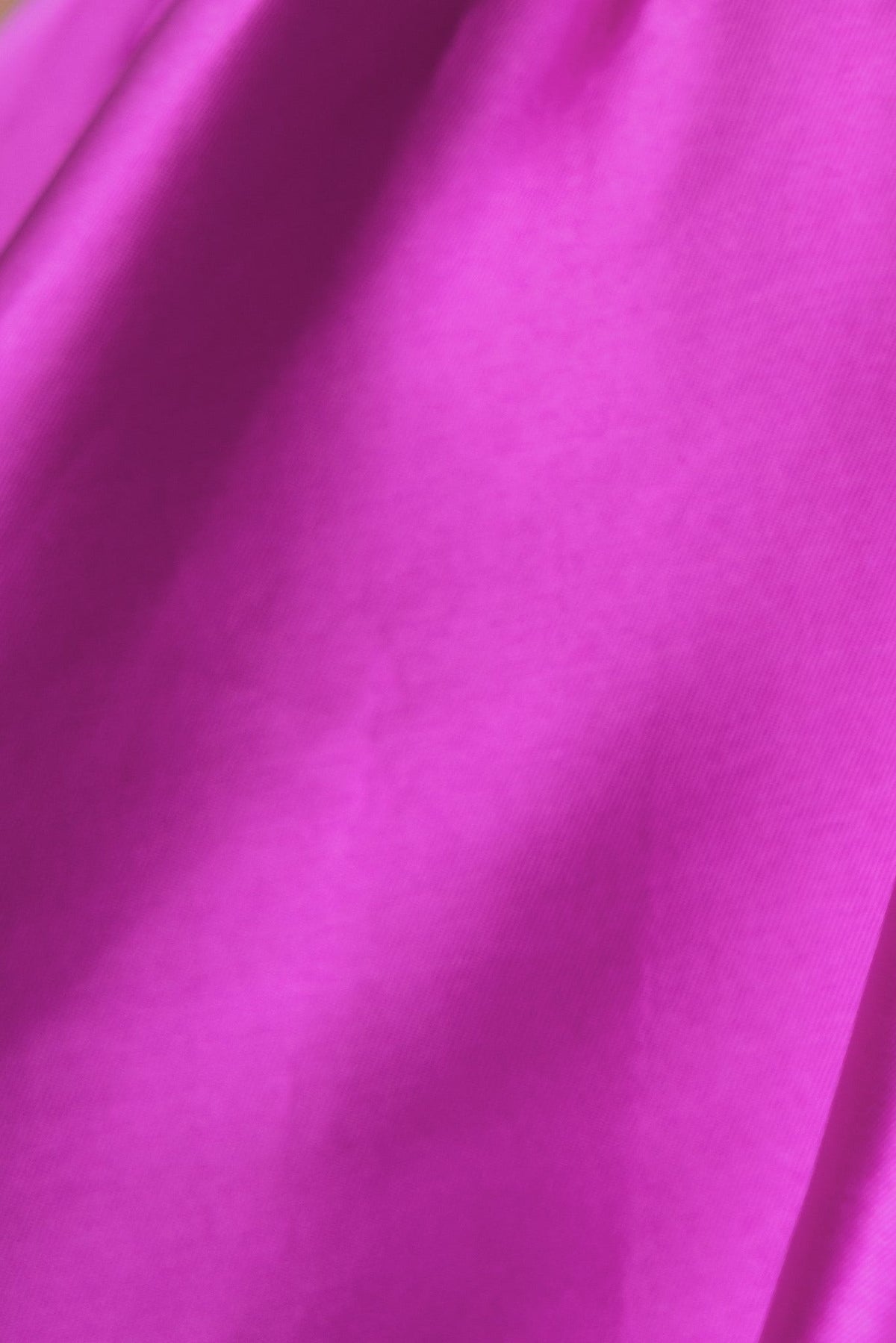 Close-up of shiny pink fabric, showcasing a vibrant hue and smooth texture, ideal for stylish dresses like the Rosebud Dress.