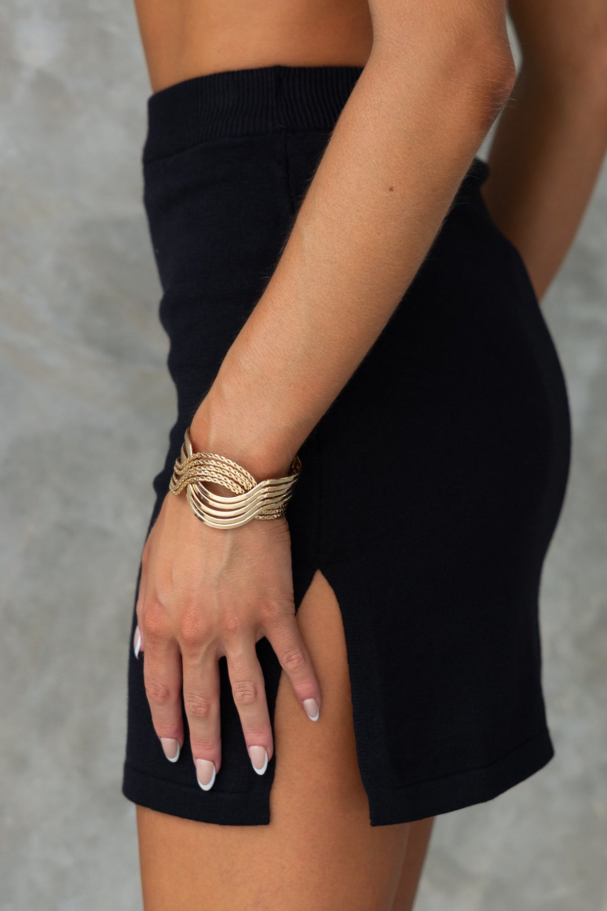 Close-up of a model wearing a black Yettie skirt with a side split and elastic waistband, paired with a gold bracelet.