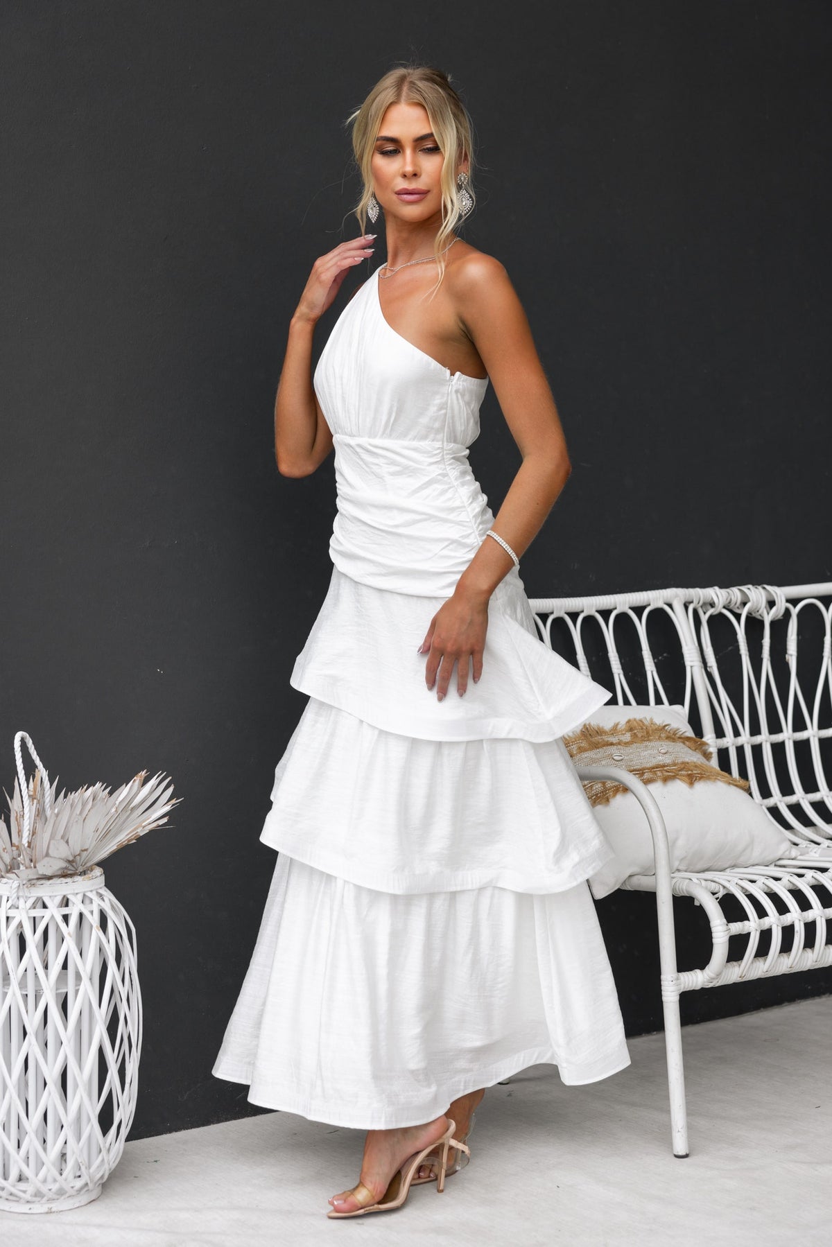 Model wearing a stylish white Bentley Maxi Dress featuring a one-shoulder design, ruffle hem, and elegant tie detail.