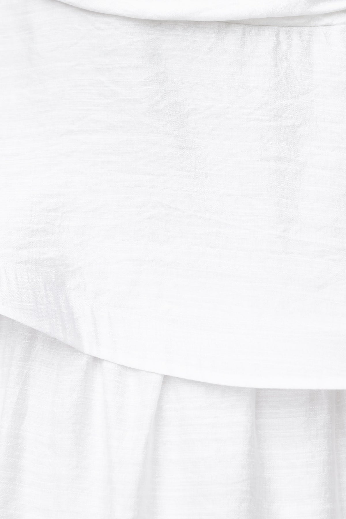 Close-up of white maxi dress fabric, featuring a ruffle hem and soft, textured material with a one-shoulder detail.