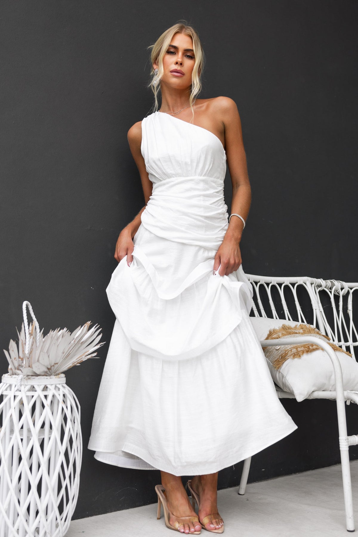 Model wearing a white Bentley Maxi Dress with one-shoulder neckline and ruffle hem against a dark background.