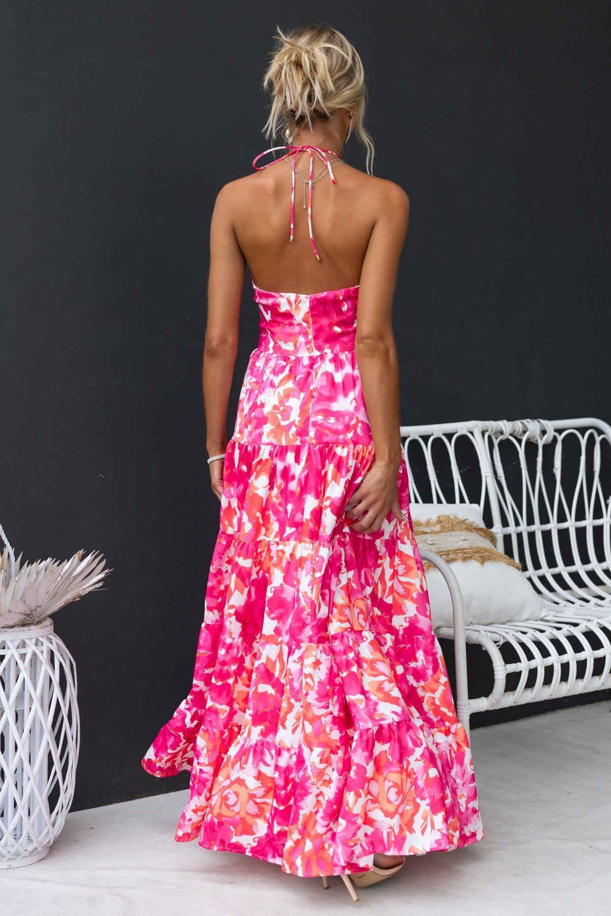Back view of a woman wearing a pink floral print Lauri maxi dress with a halter neckline and flowing skirt.