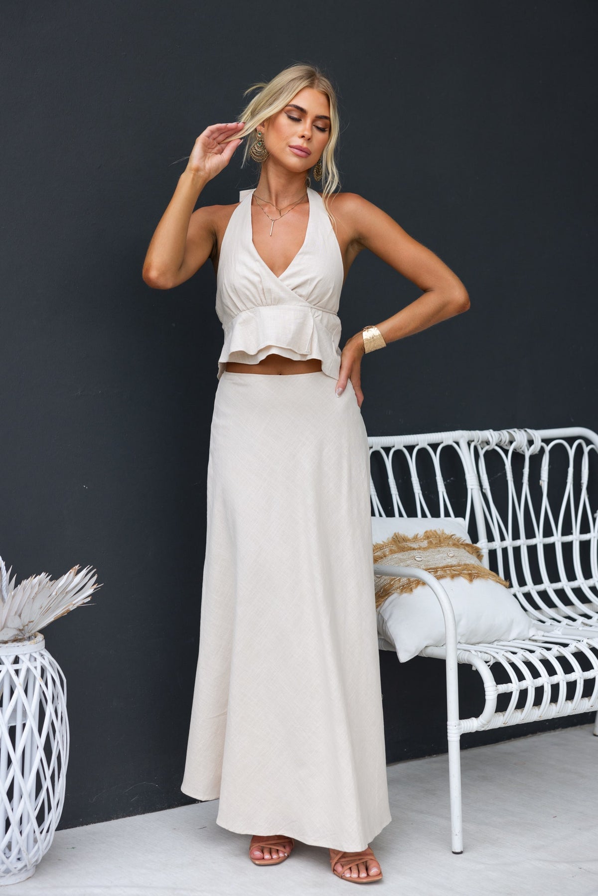 Woman wearing a Shana Maxi Skirt, styled with a beige crop top, posing elegantly beside a white wicker chair.