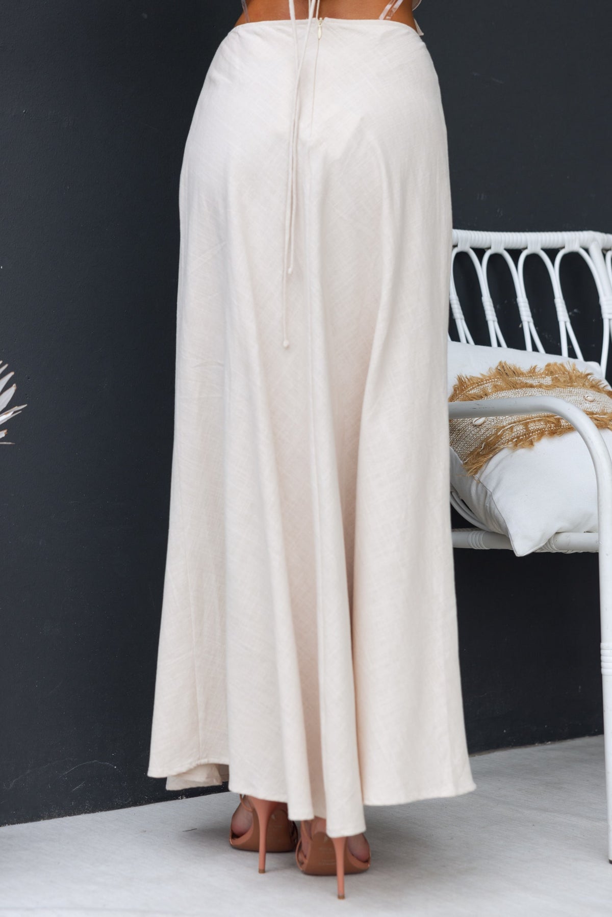 Back view of a flowy beige Shana maxi skirt with a high waist and invisible zip, styled with neutral heels.