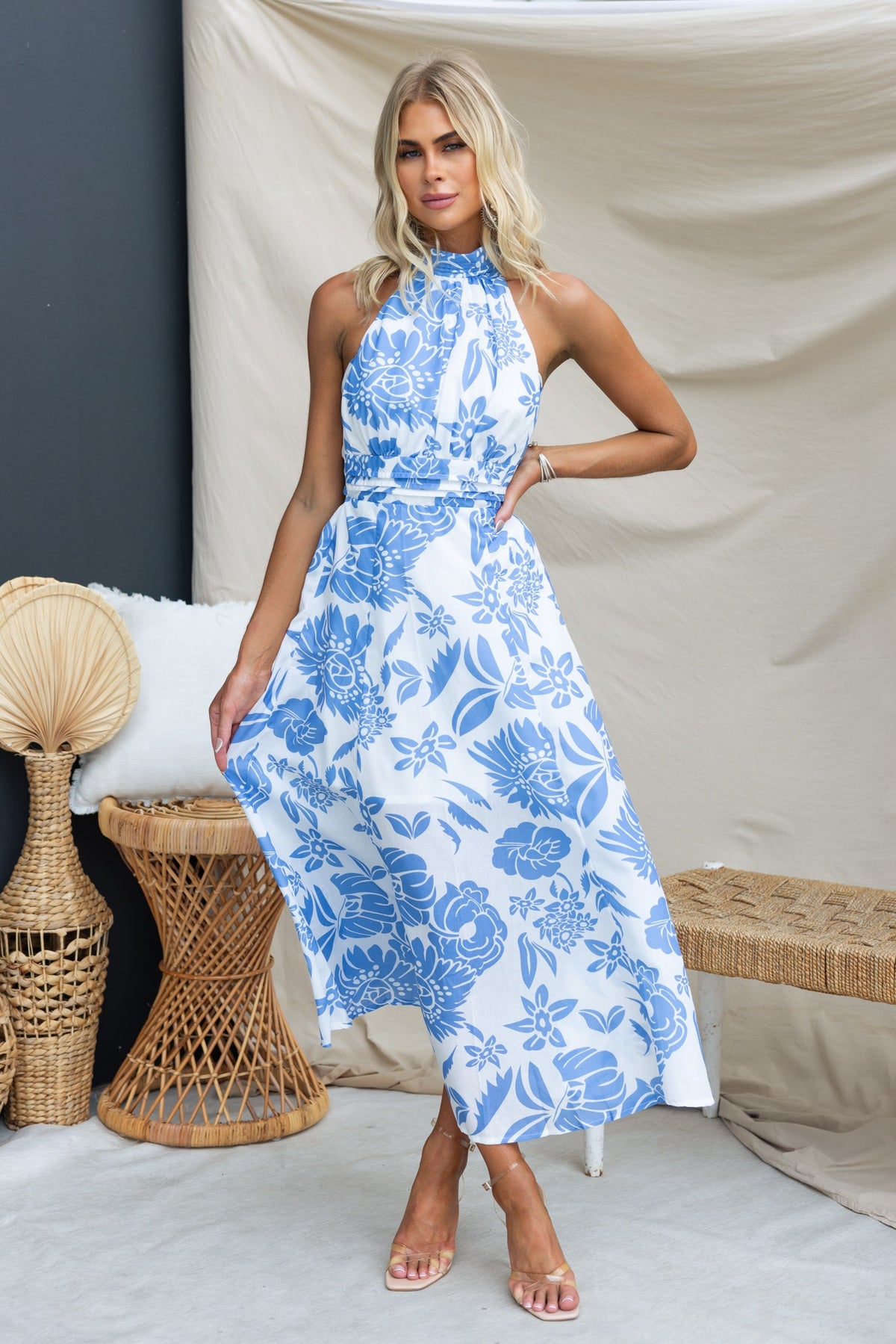 Model wearing a blue and white floral Corio Midi Dress, styled elegantly with light heels, set against a neutral backdrop.