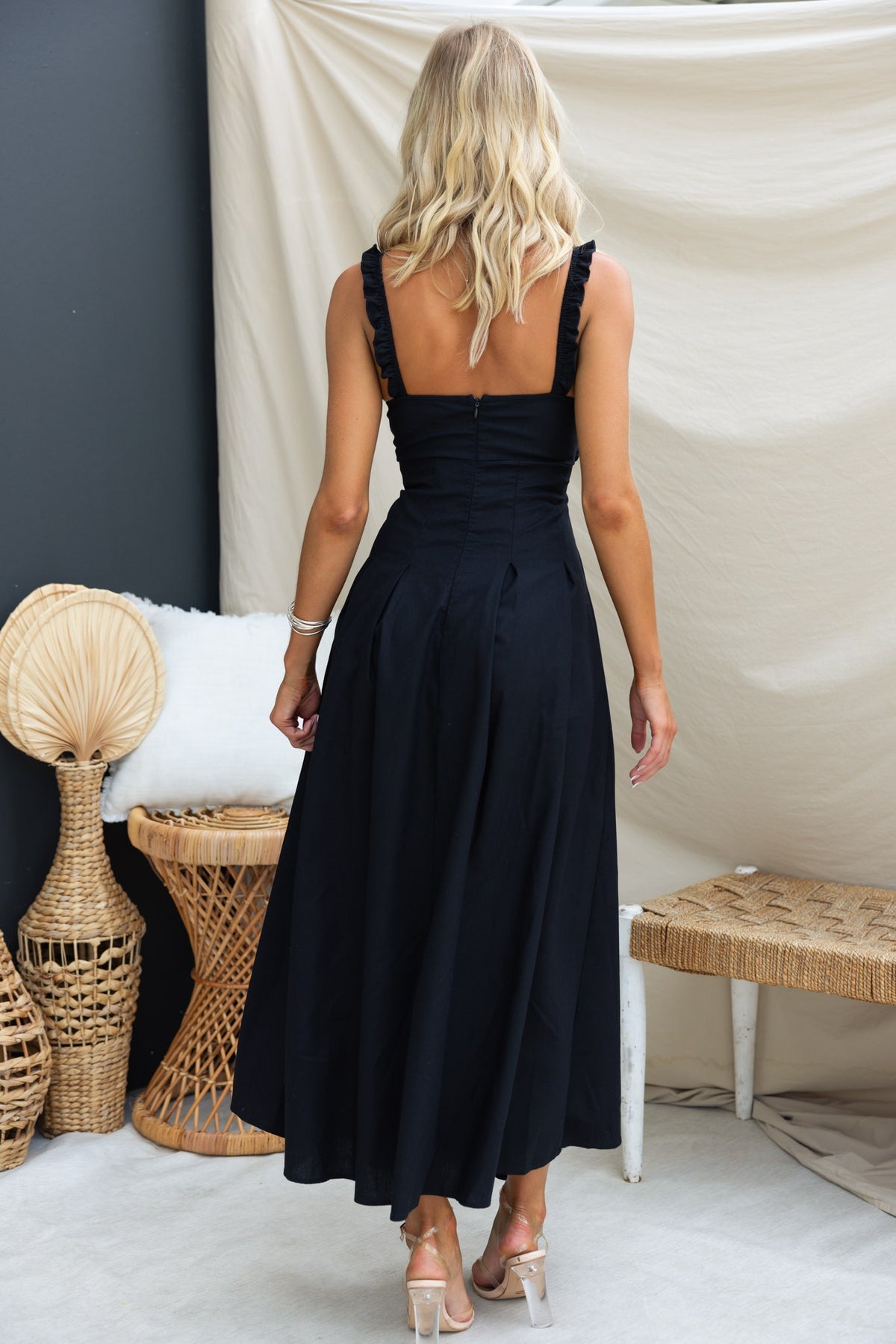 Back view of a woman in a black linen blend Nerida maxi dress with elastic straps and twist detail.