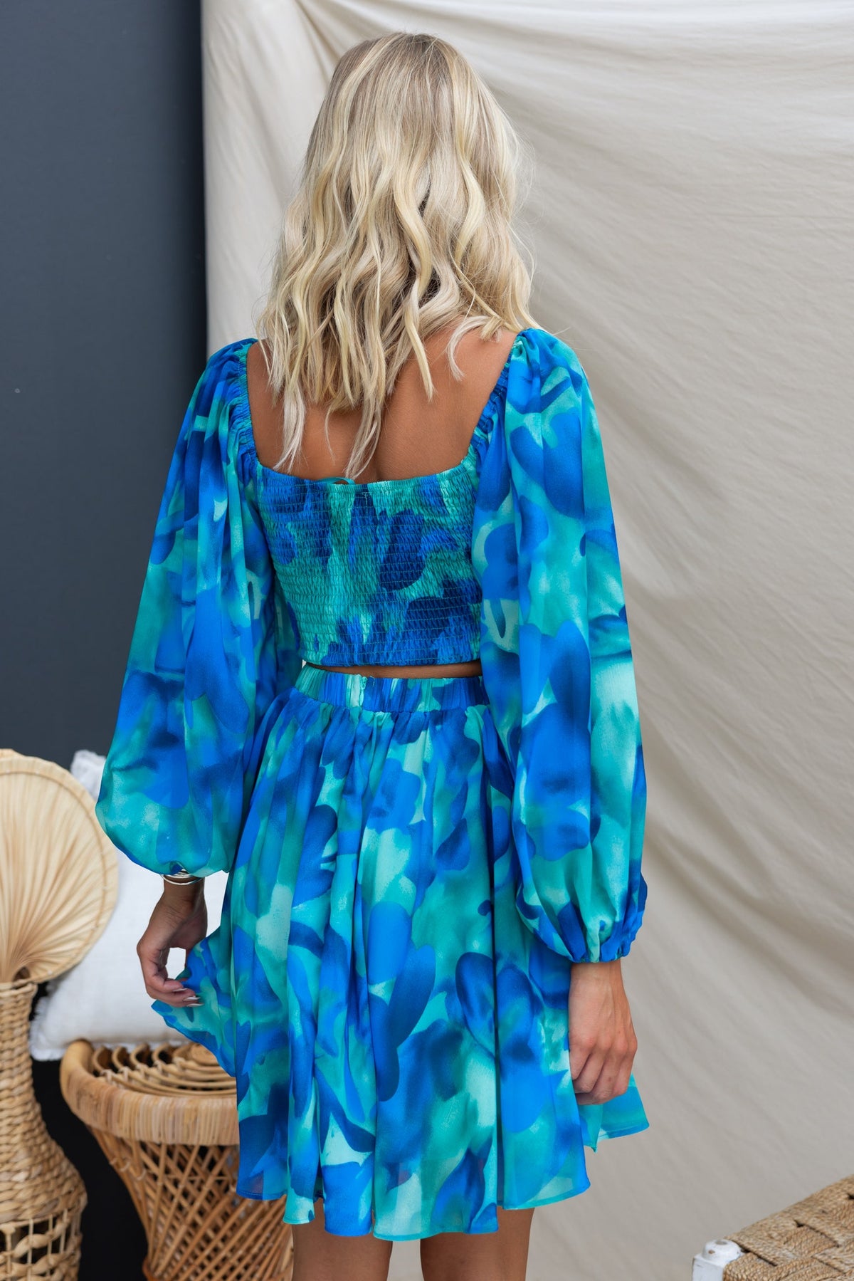 Back view of the Ellia Dress in blue-green chiffon, featuring elastic sleeves and a cut-out design, styled minimally.