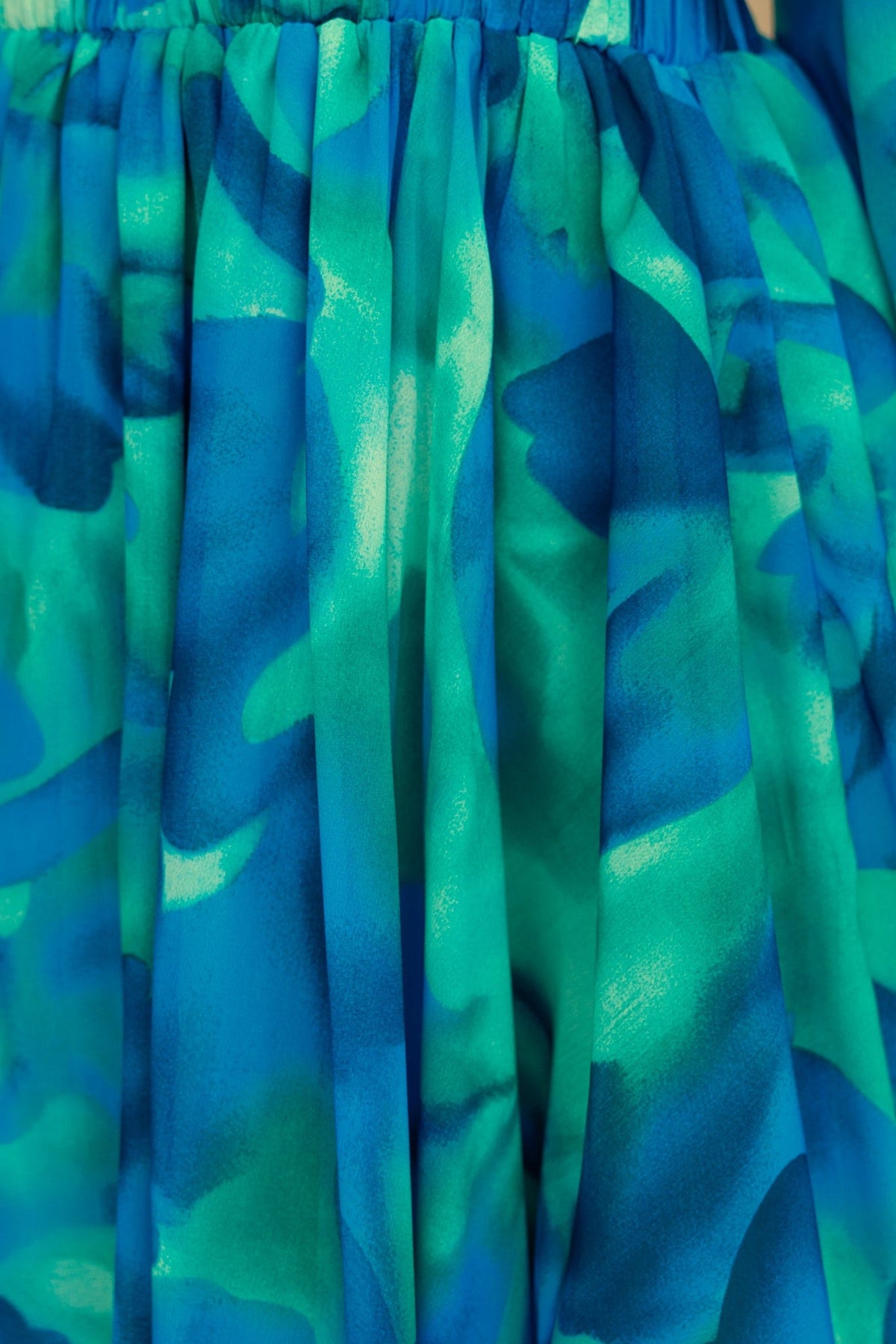 Close-up of the vibrant blue and green fabric of the Ellia Dress, showcasing pleats and chiffon texture.