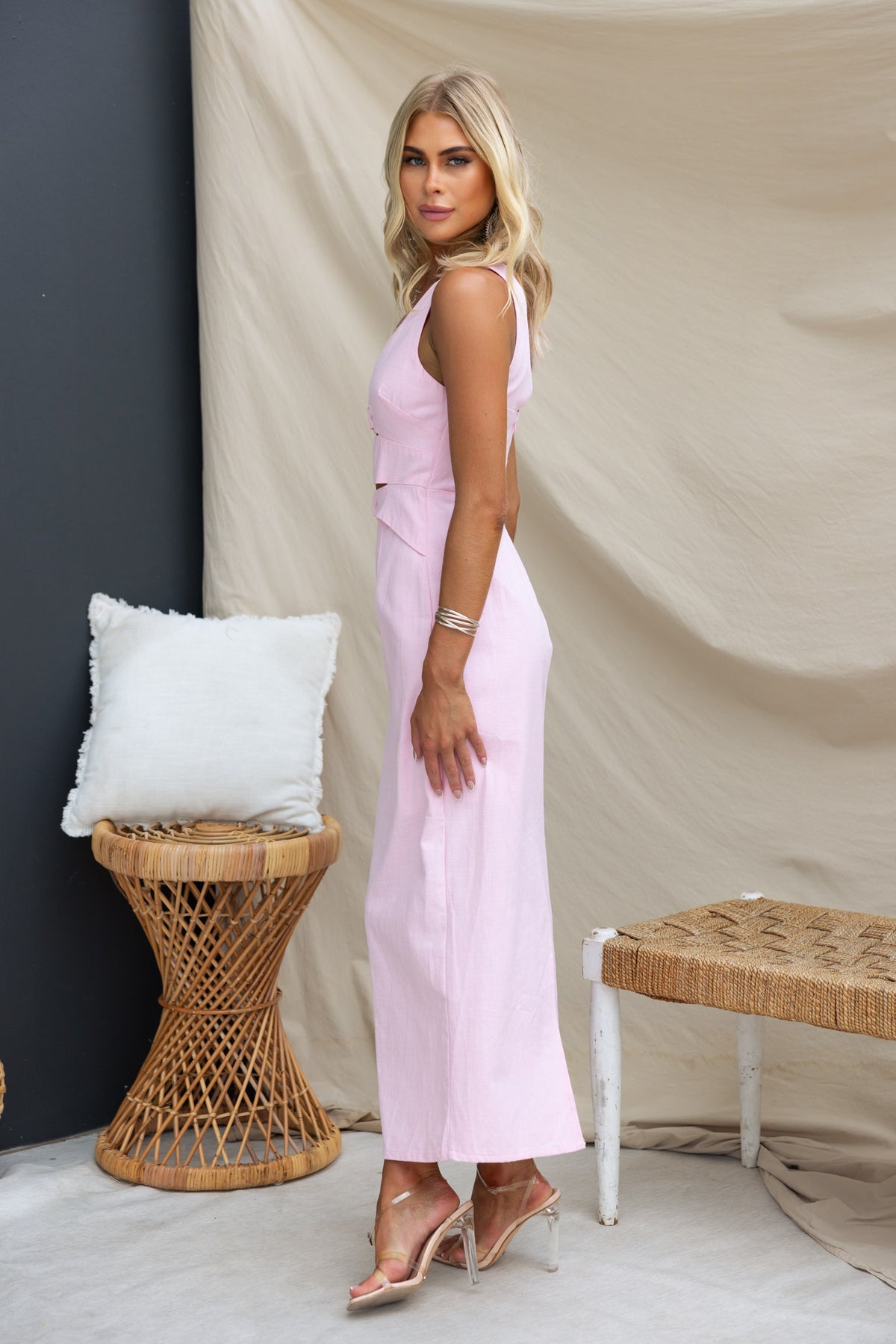 Mirai Maxi Dress in light pink, featuring a V-neckline and cut-out waist, styled in a modern setting with natural decor.