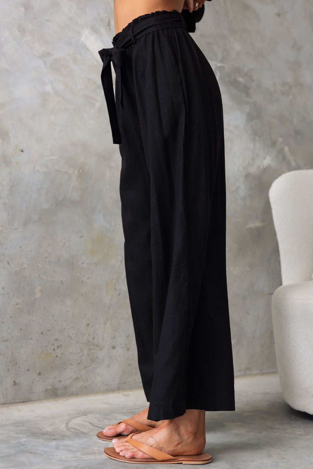 Side view of Umali Pants, featuring a mid-high waist, elastic waistband, and removable tie in a stylish black color.
