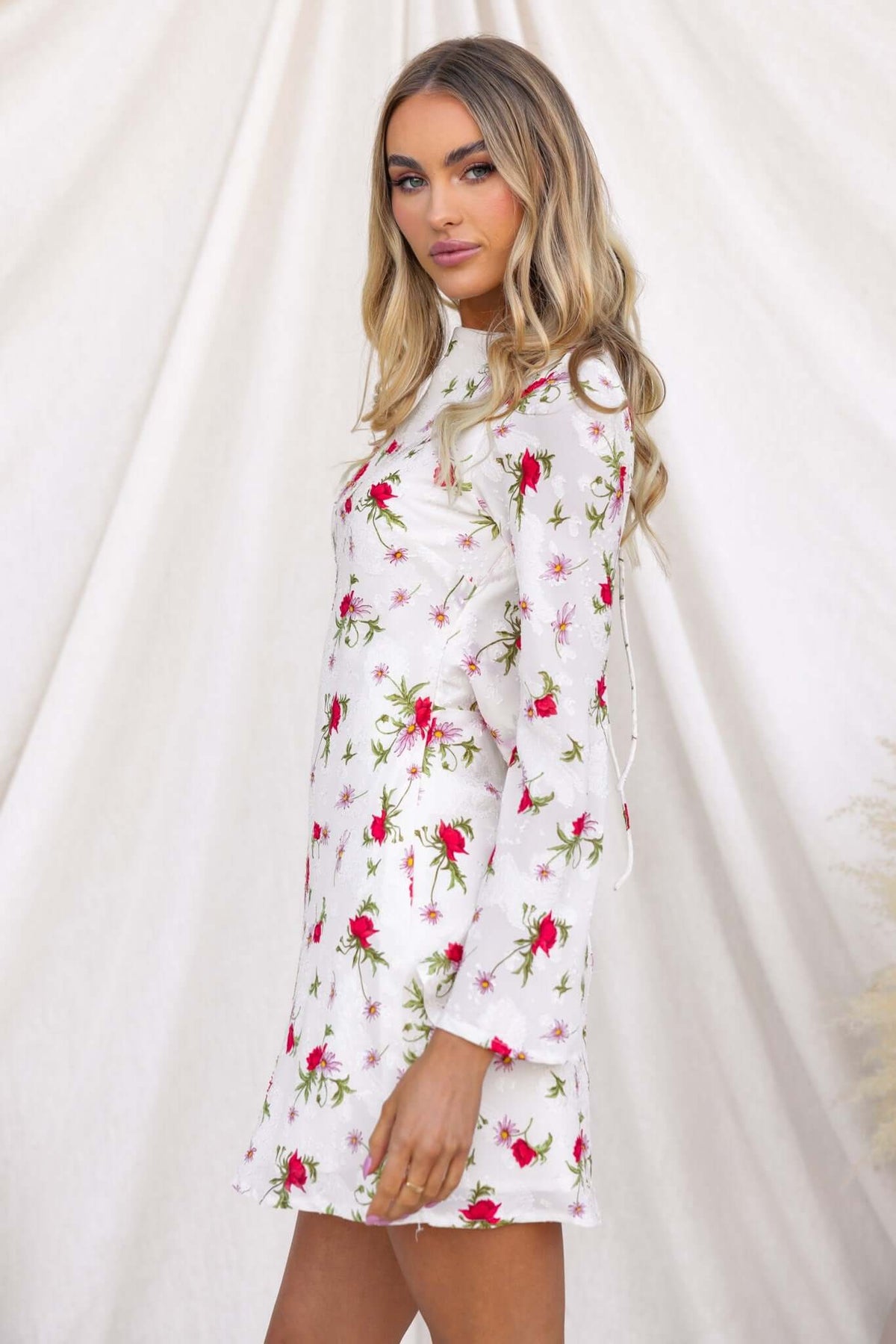 Model wearing an alluring floral print dress with long sleeves and a boat neckline against a neutral backdrop.