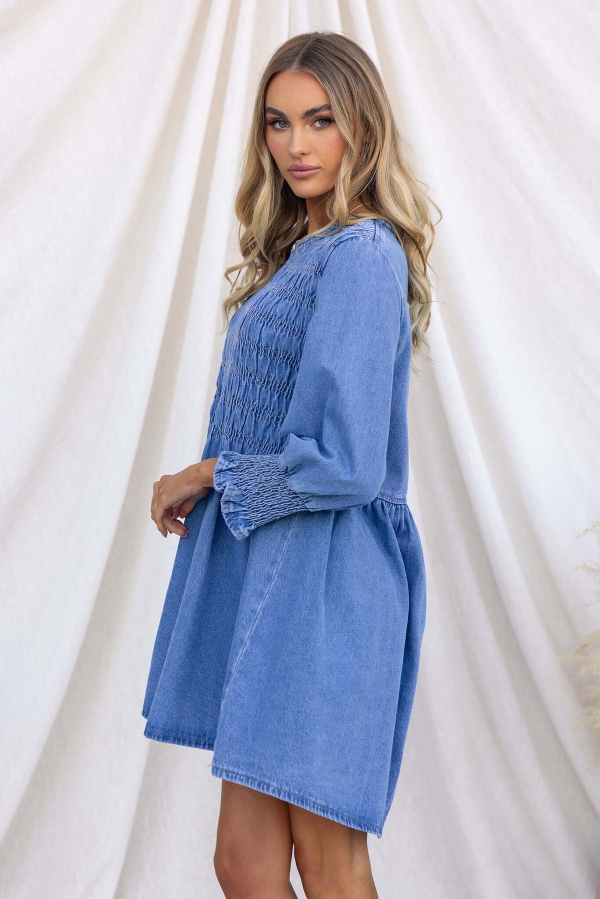 Model wearing Tulsa Denim Dress with smocked bodice and balloon sleeves, styled for a relaxed summer look.