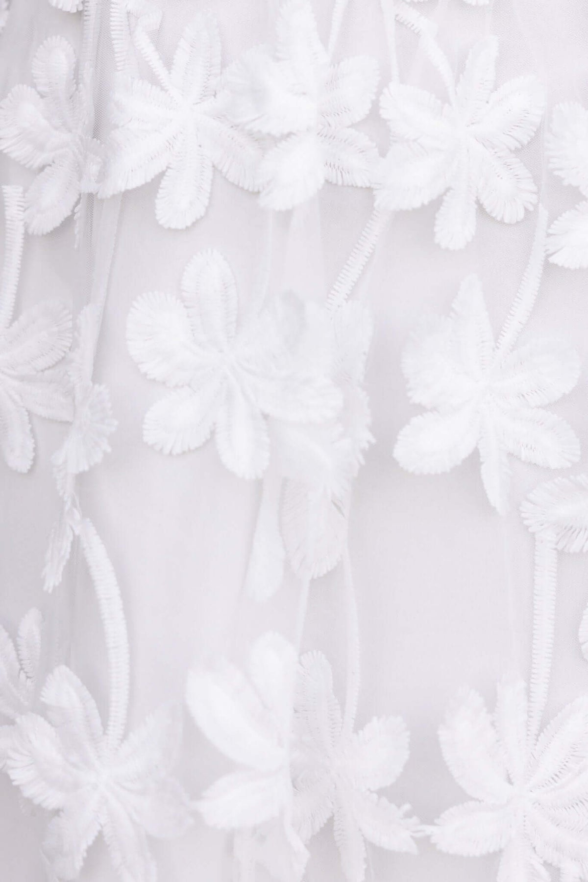 Close-up of white tulle fabric with embroidered floral design, featuring delicate flowers for elegant dress detailing.