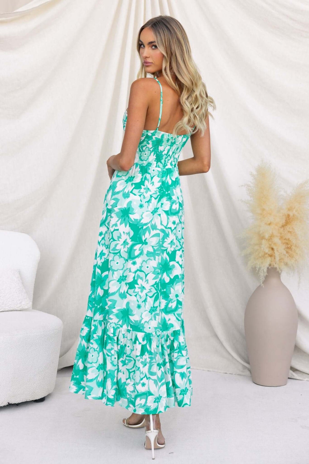 Back view of a woman in a green floral Elmira maxi dress with adjustable straps and tiered hem.