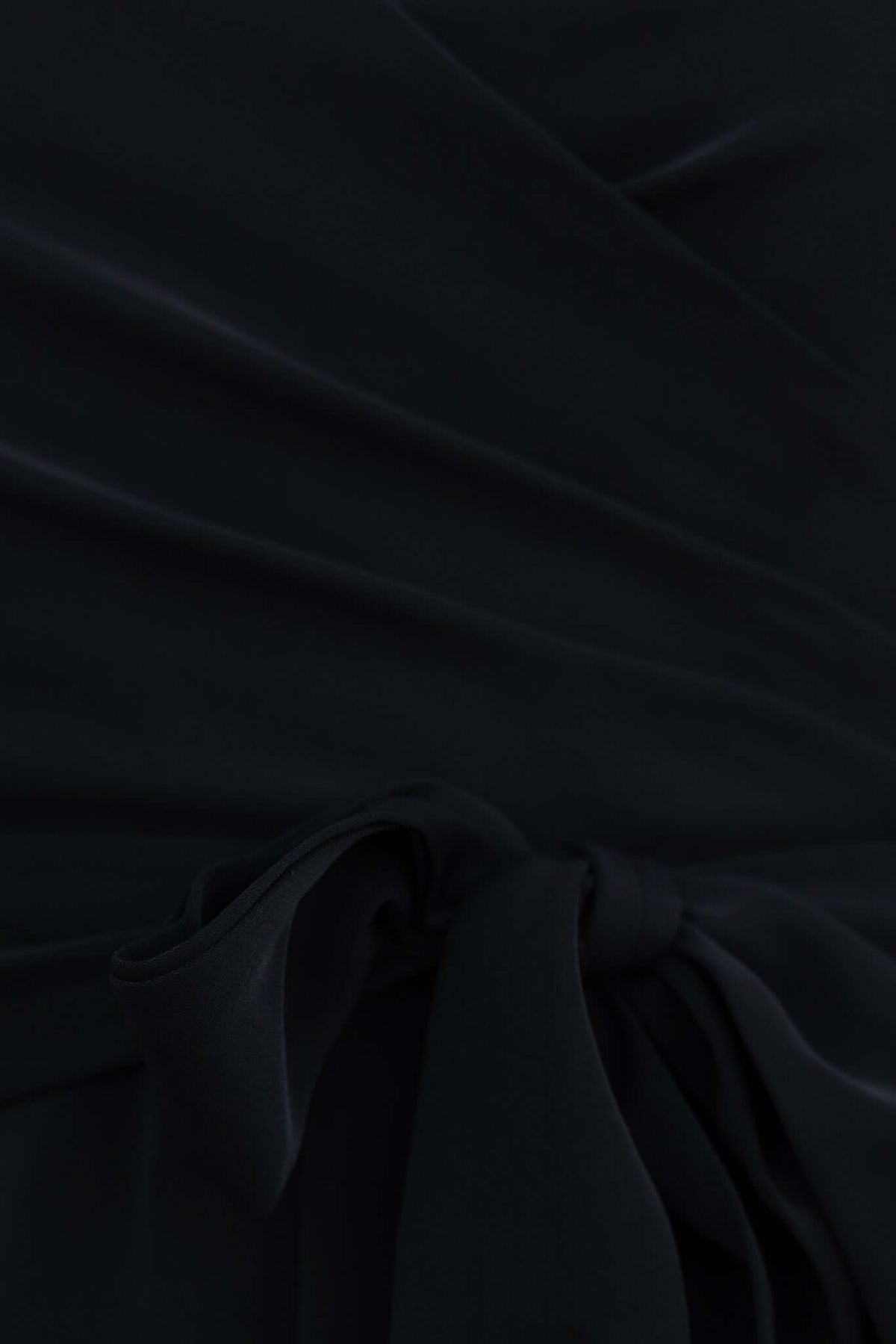 Close-up of the Couver Jumpsuit in black showcasing the tied waist detail and smooth fabric.