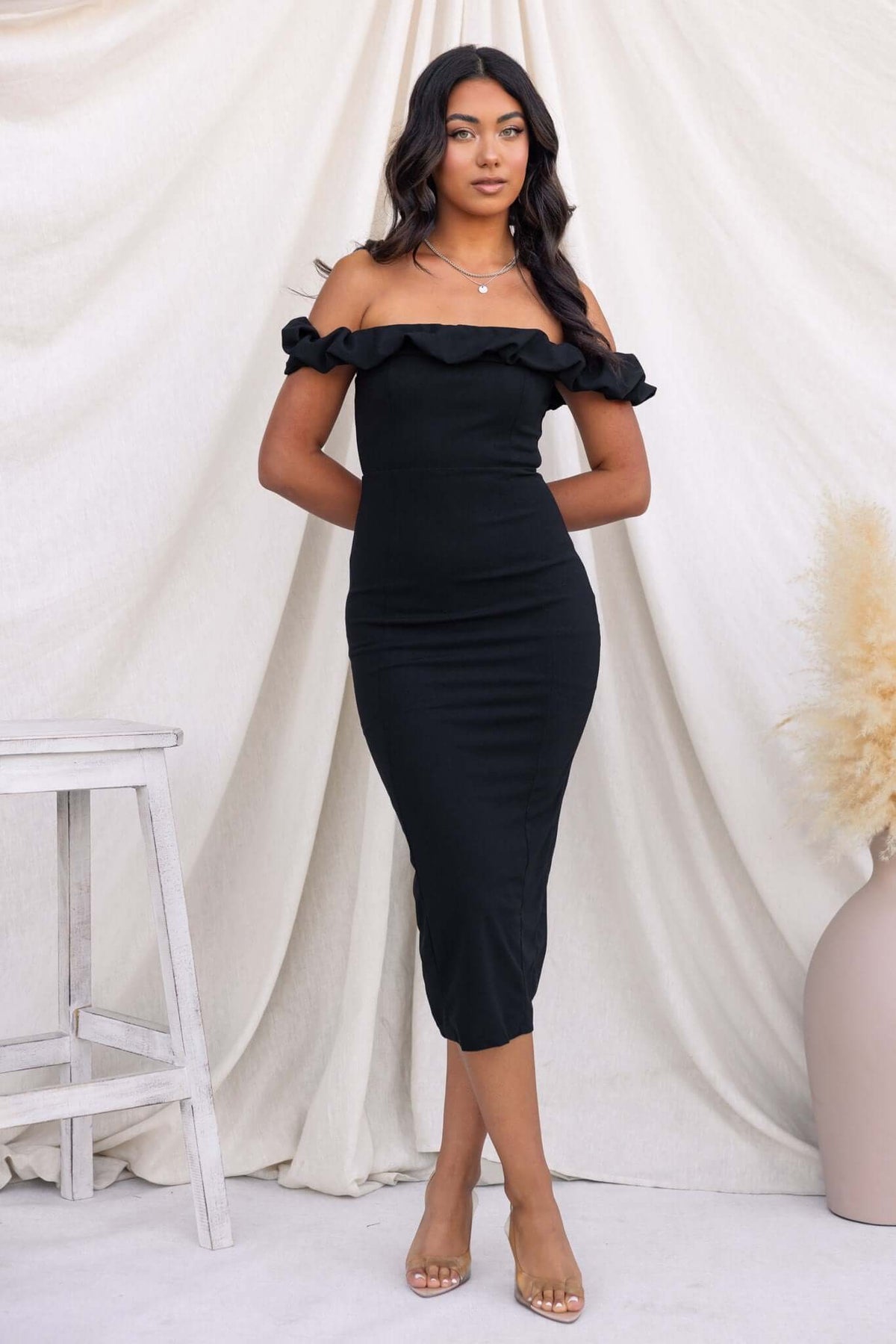 Stresa Midi Dress in black, off-shoulder style with ruffles and back split, modeled by a woman, chic and elegant.
