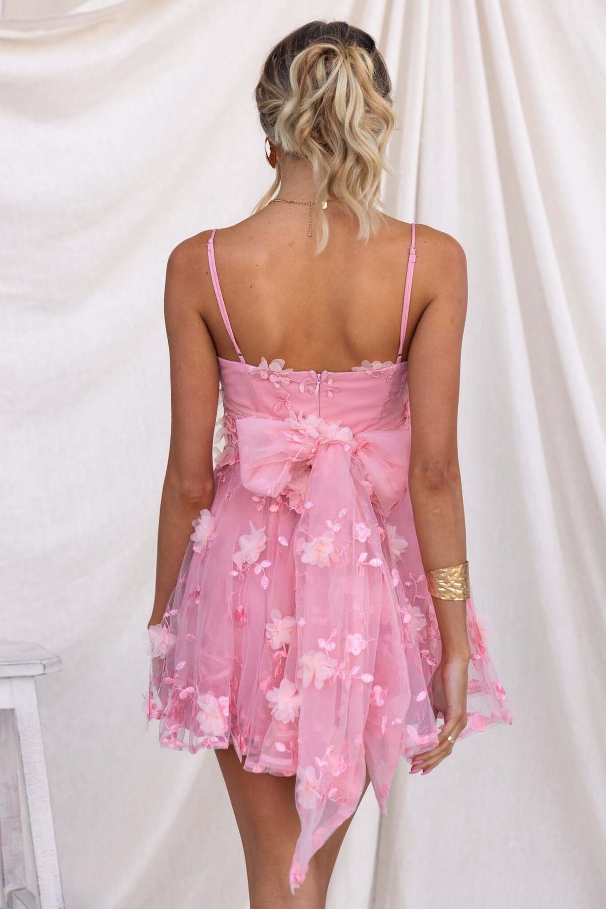 Back view of the Oh Please Dress featuring floral lace, adjustable straps, and a tied bow in soft pink fabric.