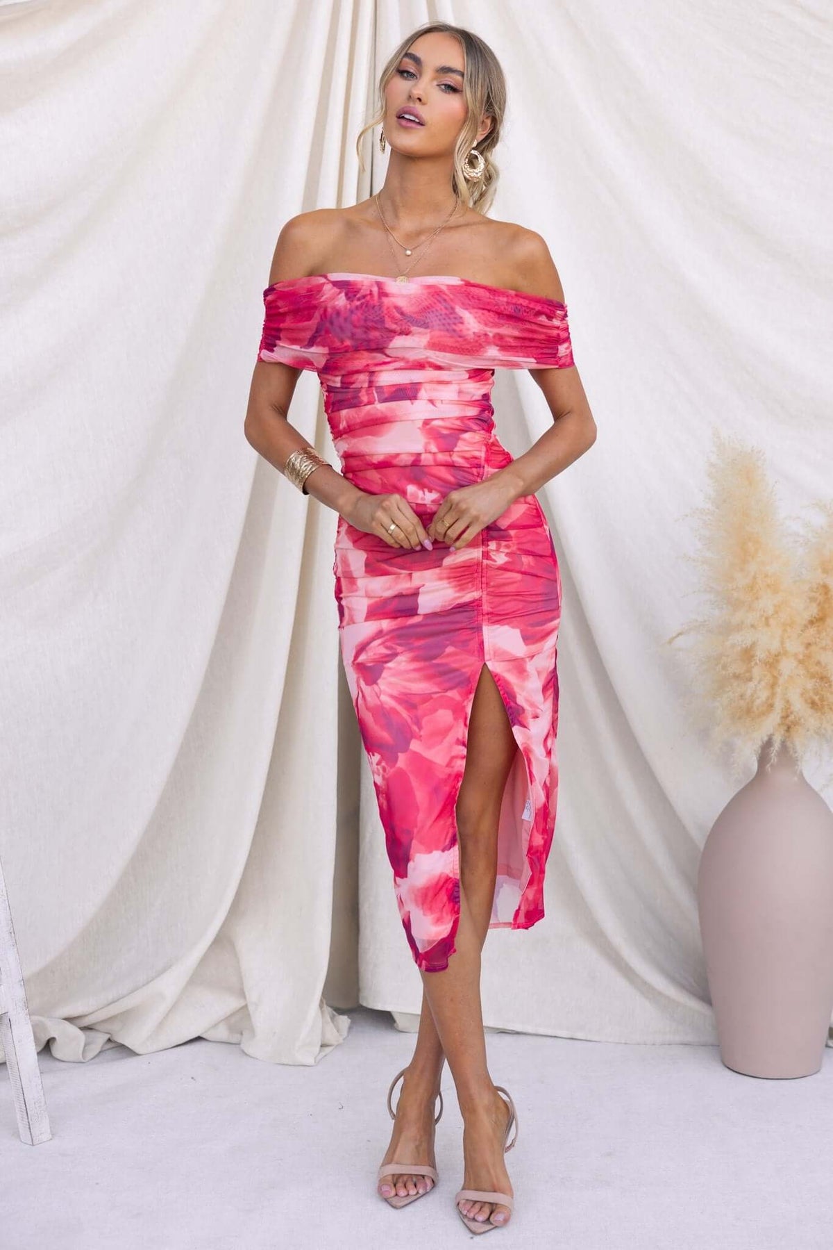 Model wearing Talinga Midi Dress with off-shoulder neckline and asymmetric hemline in vibrant pink print.