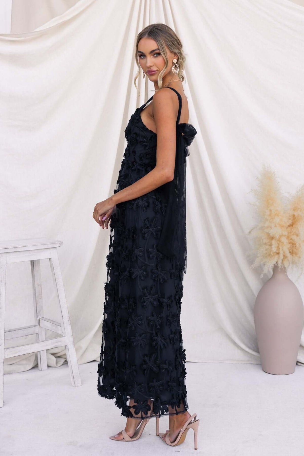 Model wearing a black Xaria maxi dress with tie straps and tulle embroidery standing elegantly.