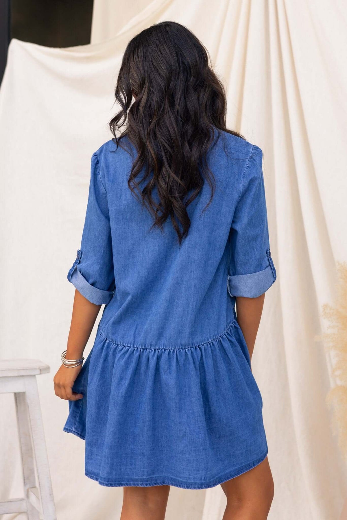 Back view of a woman in a Gracie Denim Dress with V-neckline and button-up front, showcasing relaxed fit and denim wash.