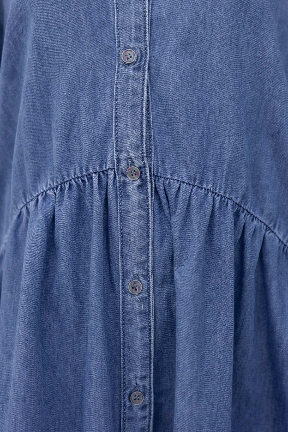 Close-up of Gracie Denim Dress featuring a V-neckline and button-up front in light blue denim fabric.