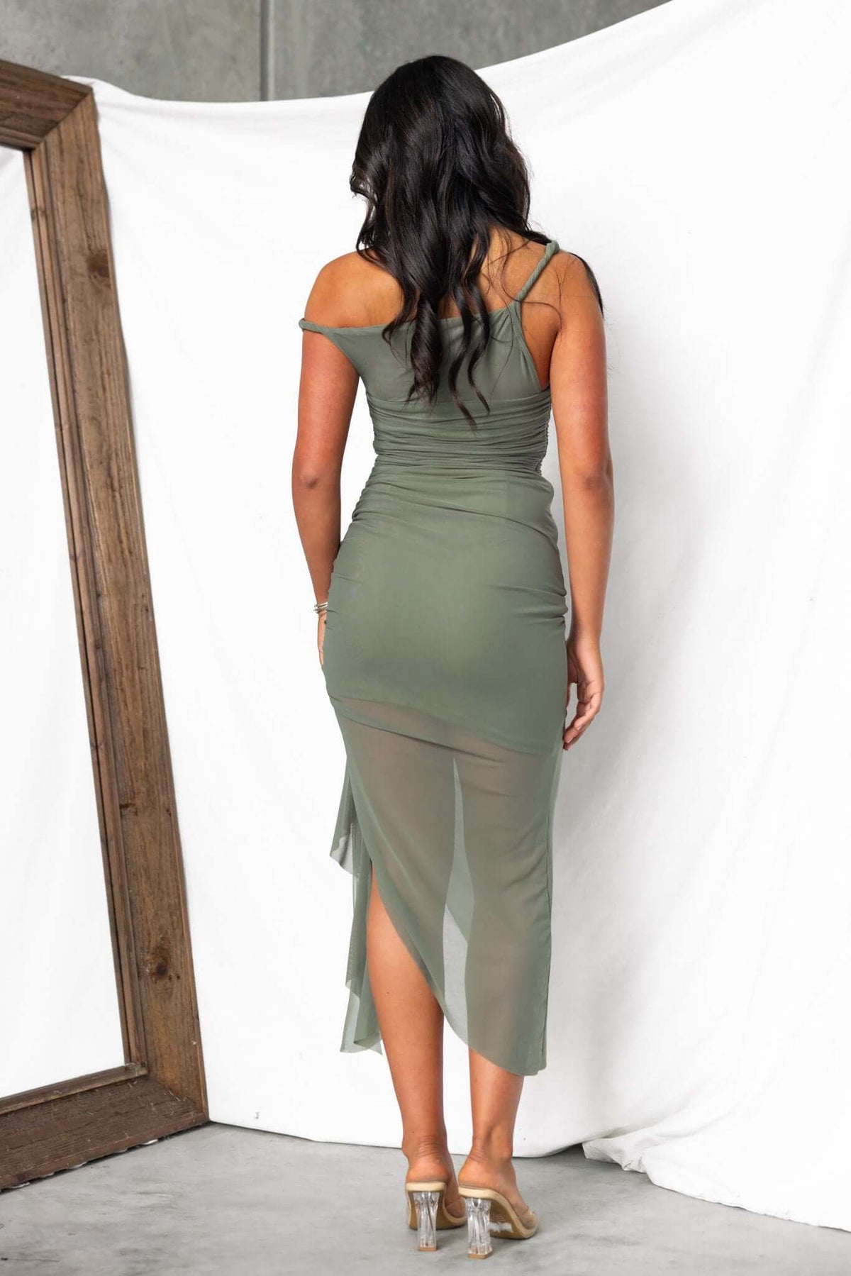 Woman in olive green Iroha Maxi Dress showcasing twist straps and asymmetric hem, with ruffle detail and mesh material.