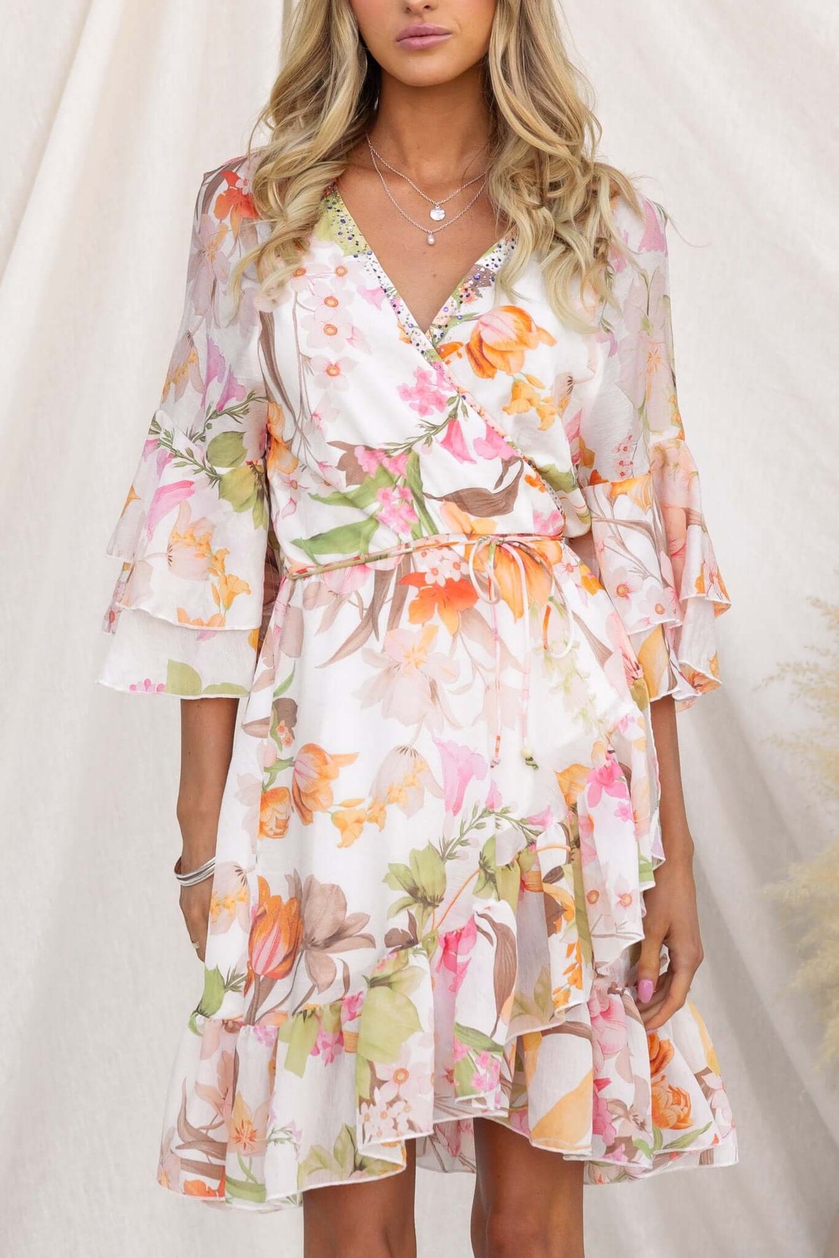 Model wearing a floral Fools Gold Wrap Dress with V-neckline, ruffled sleeves, and gem embellishments.