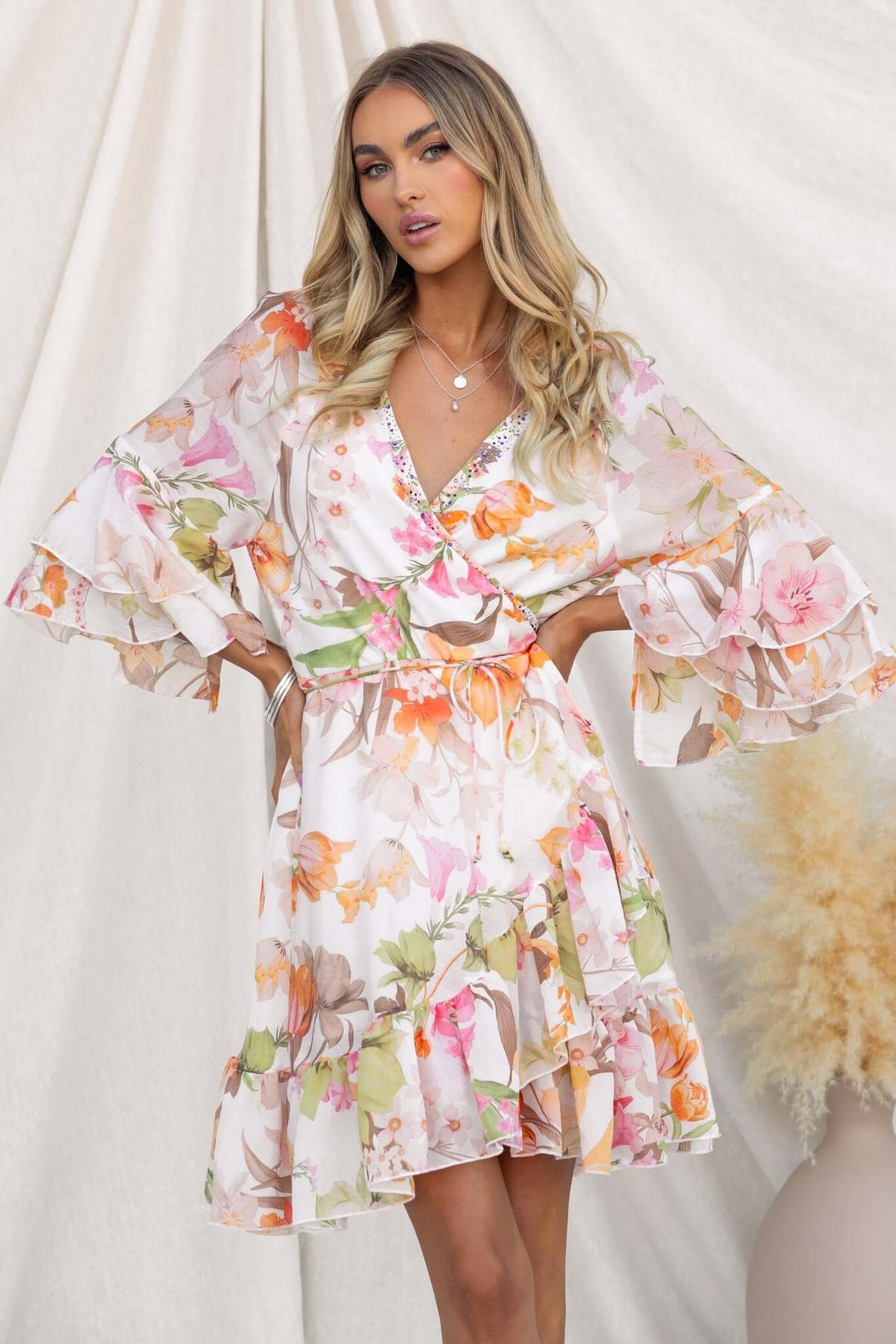 Model wearing the Fools Gold Wrap Dress with floral pattern and bell sleeves, showcasing a V-neckline and tie detail.