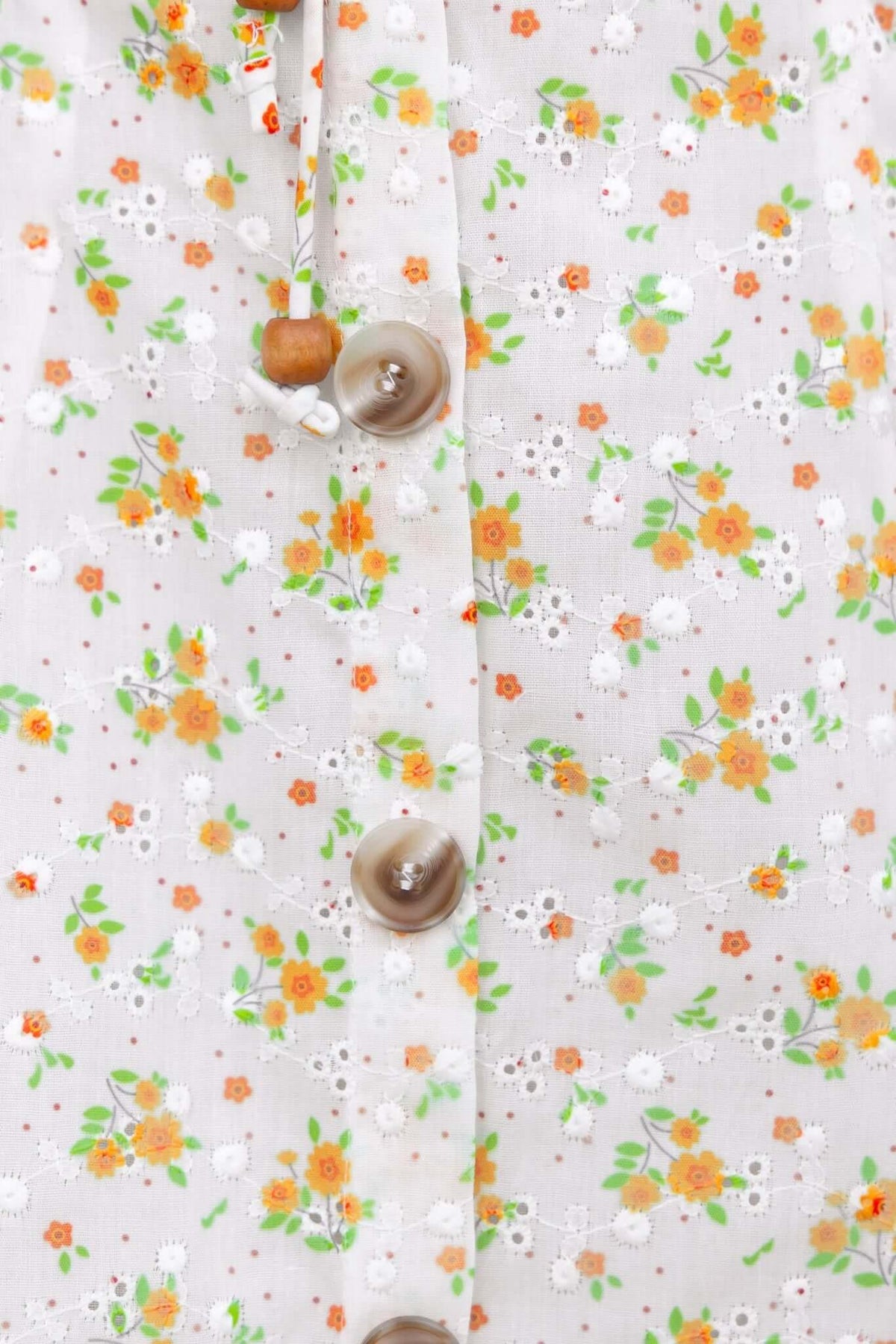 Close-up of a floral dress fabric featuring orange and white flowers with faux buttons for a charming look.