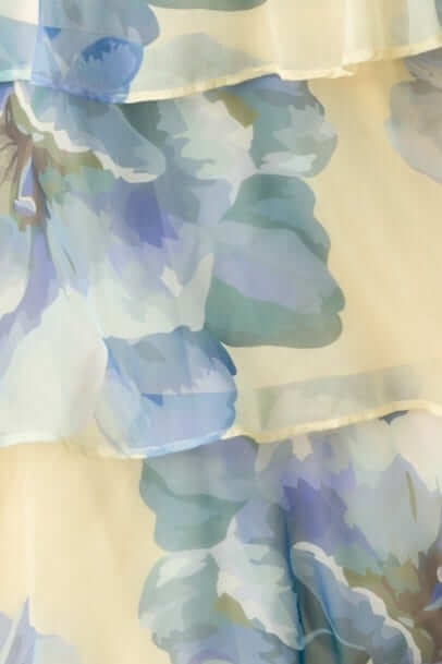 Close-up of a flowing maxi dress featuring a soft floral pattern in light blues and yellows, highlighting the chiffon texture.
