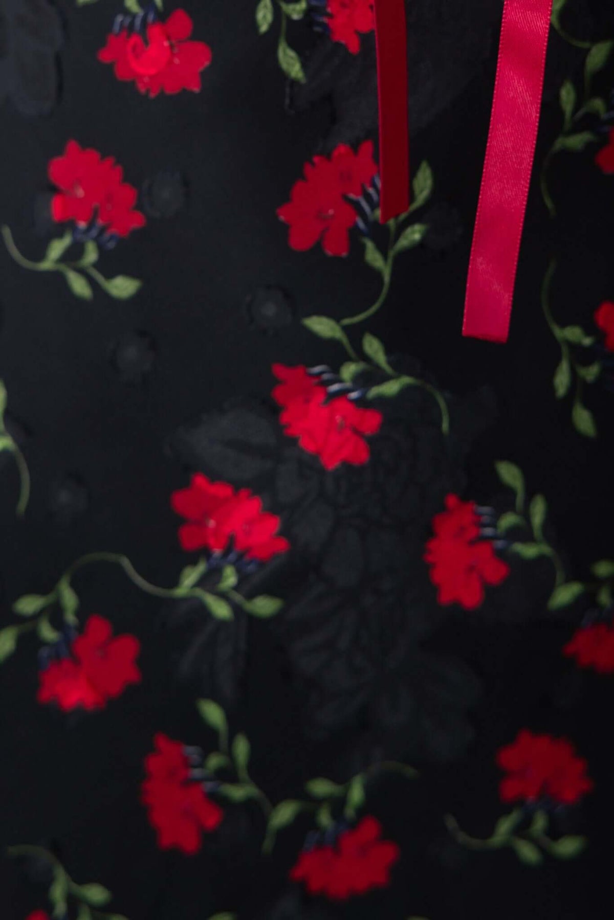 Close-up of black fabric featuring vibrant red flowers and green leaves, with a decorative pink ribbon.