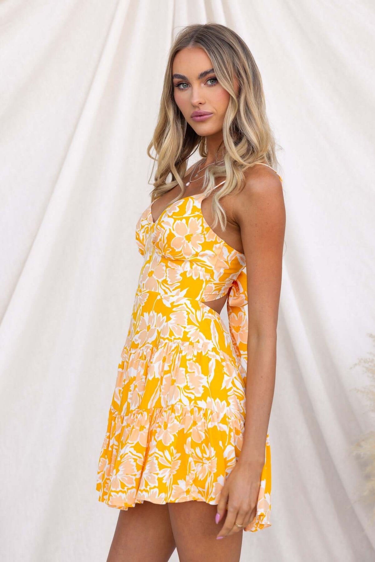 Model wearing the Everton Dress in vibrant yellow floral print, featuring adjustable straps and a flared skirt.