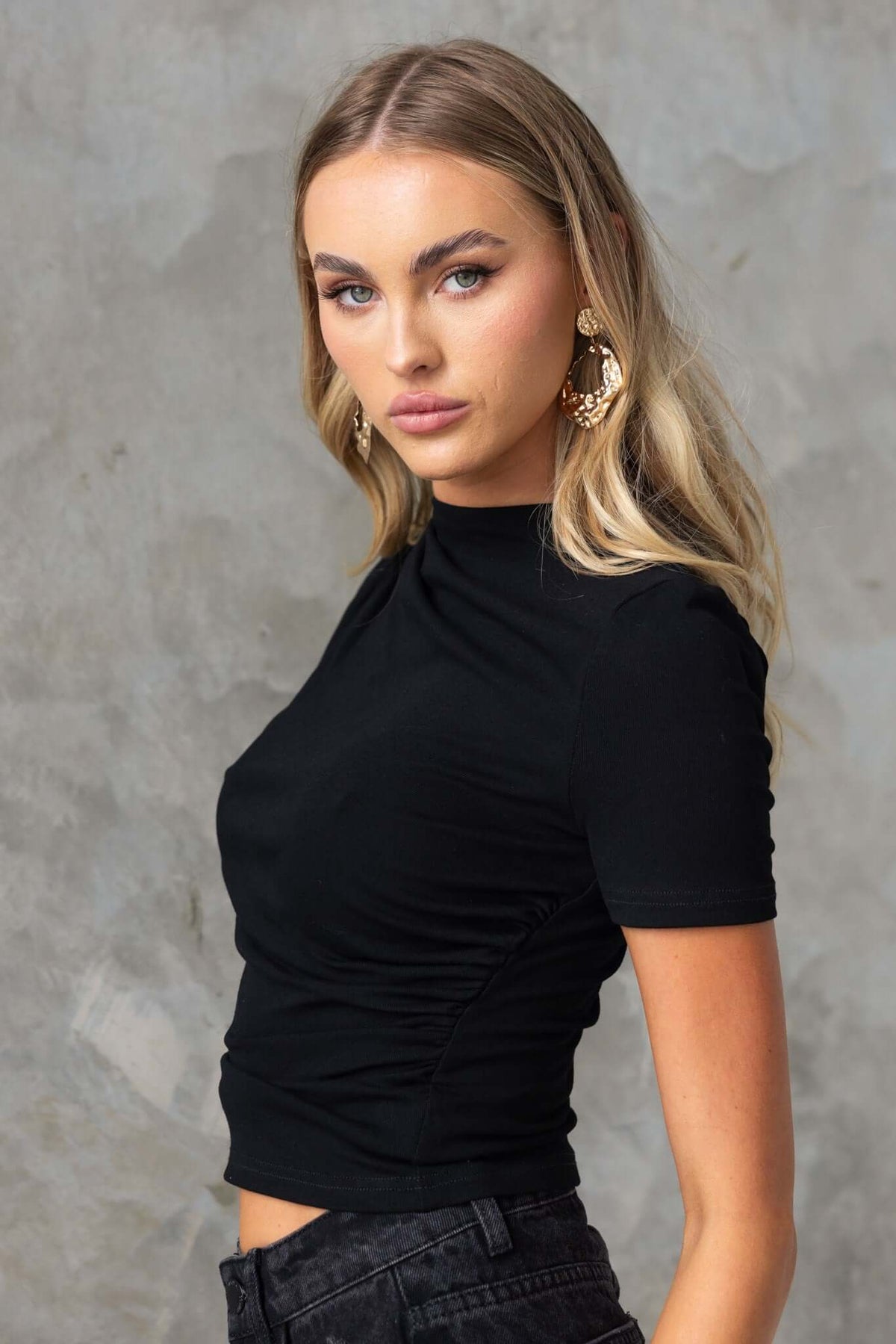 Model wearing a black Icon Top with round neckline and ruching details, showcasing a stylish summer outfit.