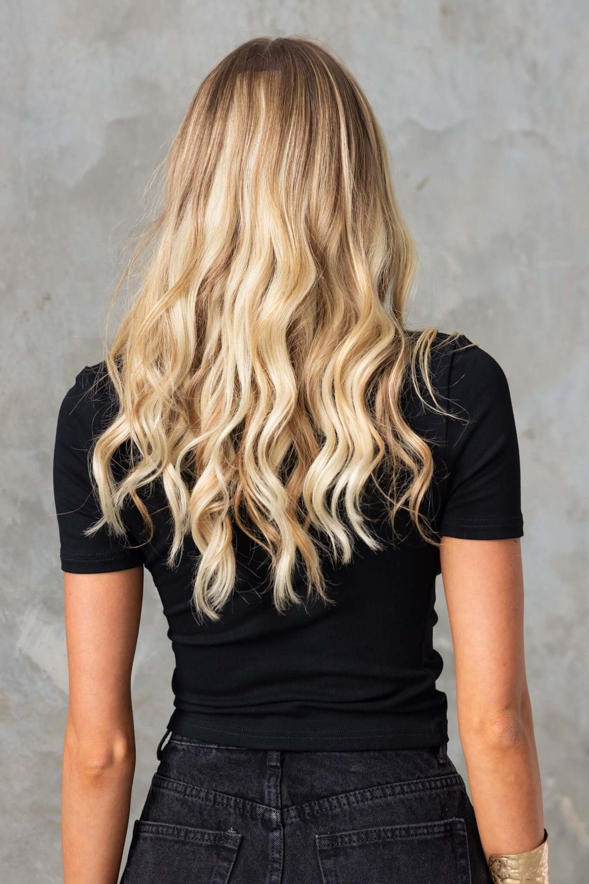 Model showcasing the back of a black top with wavy blonde hair, styled with a relaxed look.