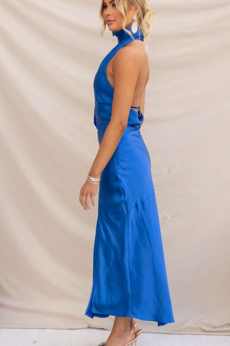 Side view of a woman in a blue Havenah maxi dress, featuring a wrap neck design and sleek satin finish.