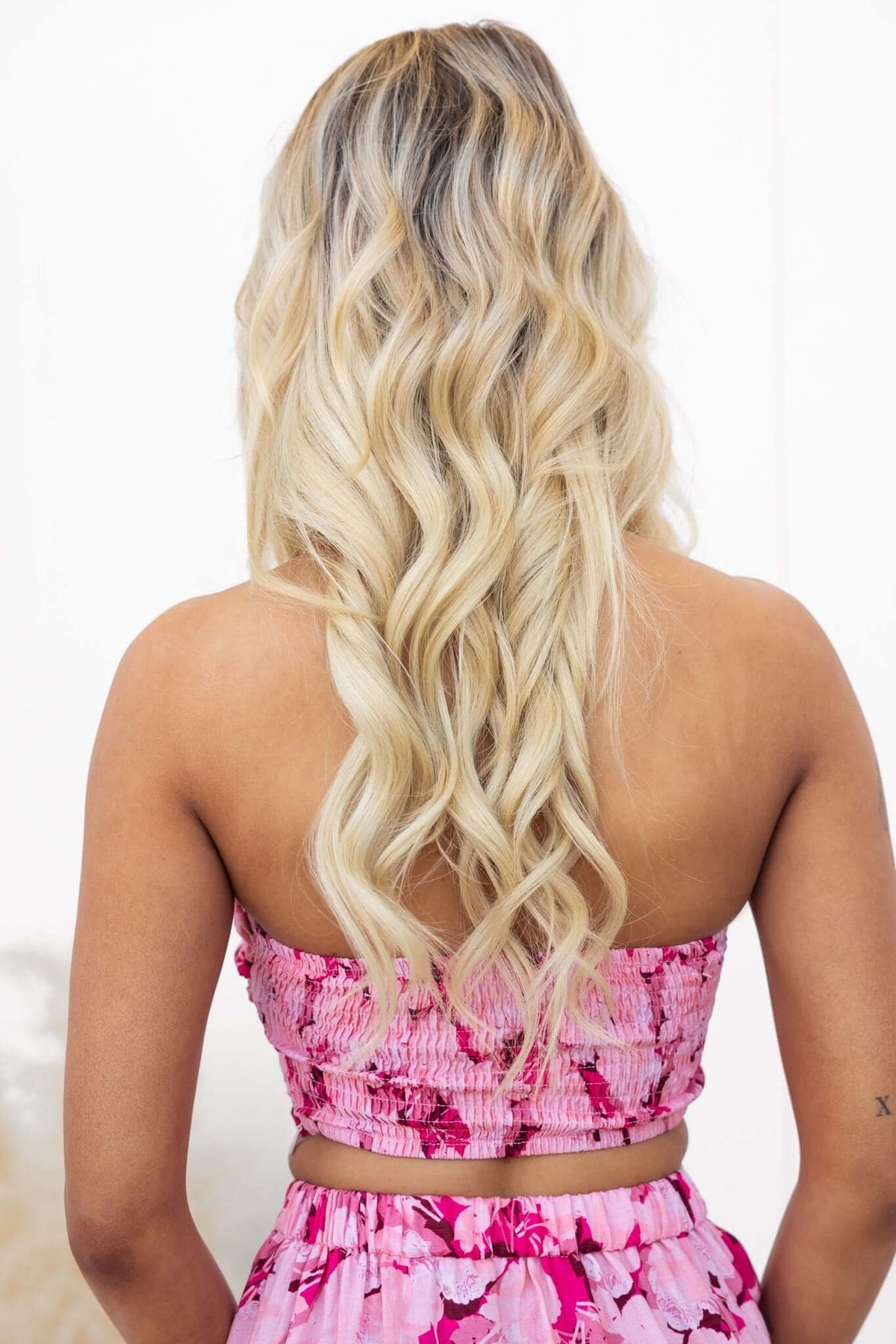 Back view of a model wearing a pink floral top with shirred details and wavy blonde hair.