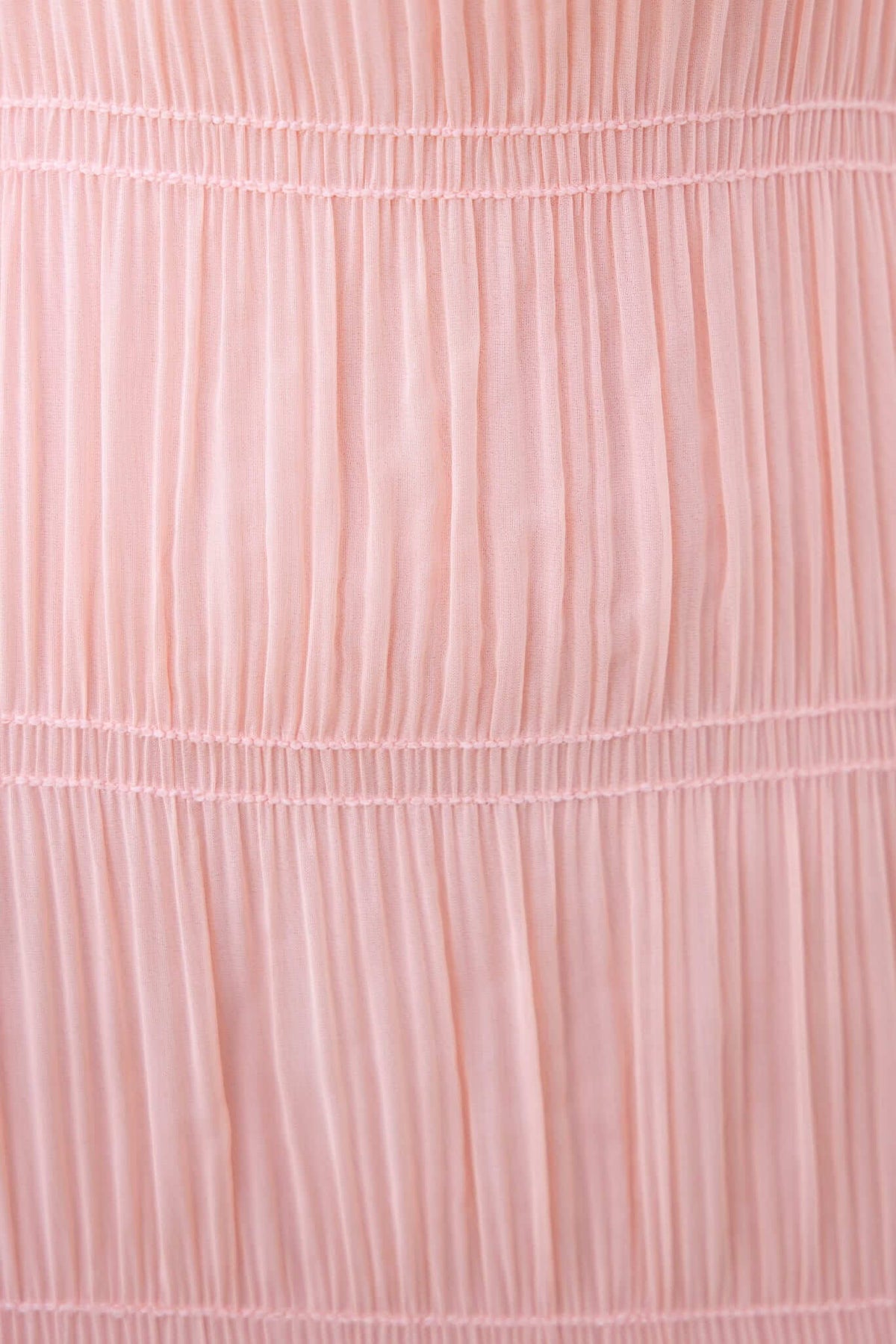 Close-up of soft pink maxi dress fabric with delicate pleats and stitching, showcasing luxurious texture and flow.