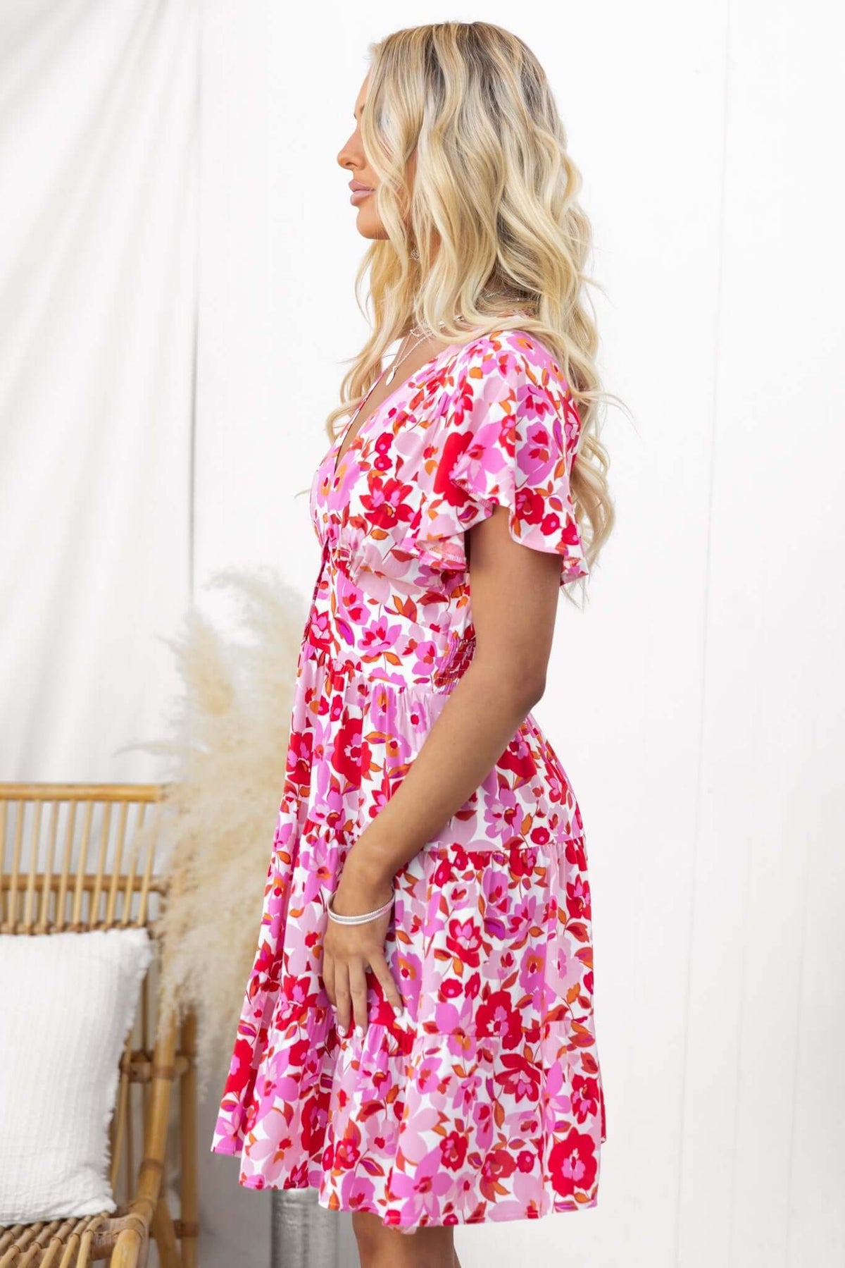 Side view of a model in a vibrant pink floral mini dress with ruffled sleeves, perfect for summer outings.