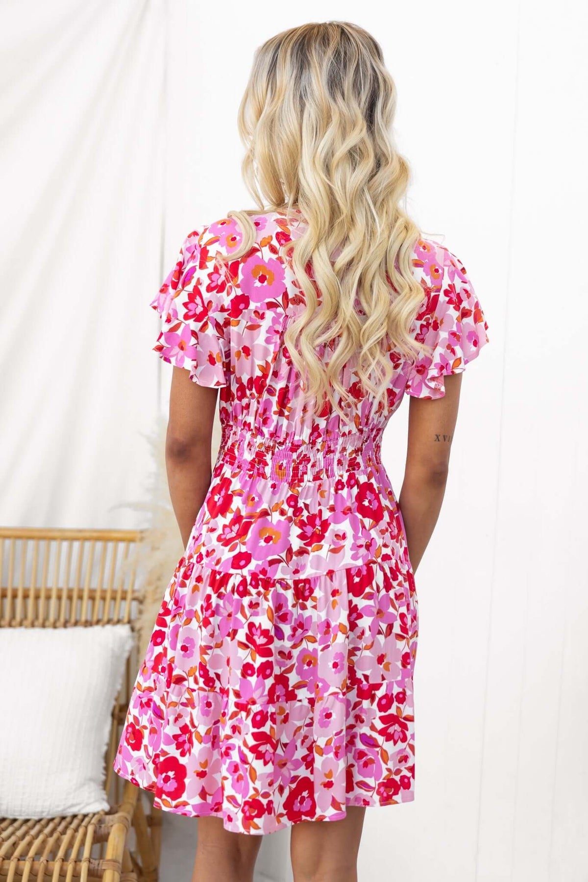 Back view of a model in a pink floral mini dress with ruffled sleeves, styled with loose blonde waves.