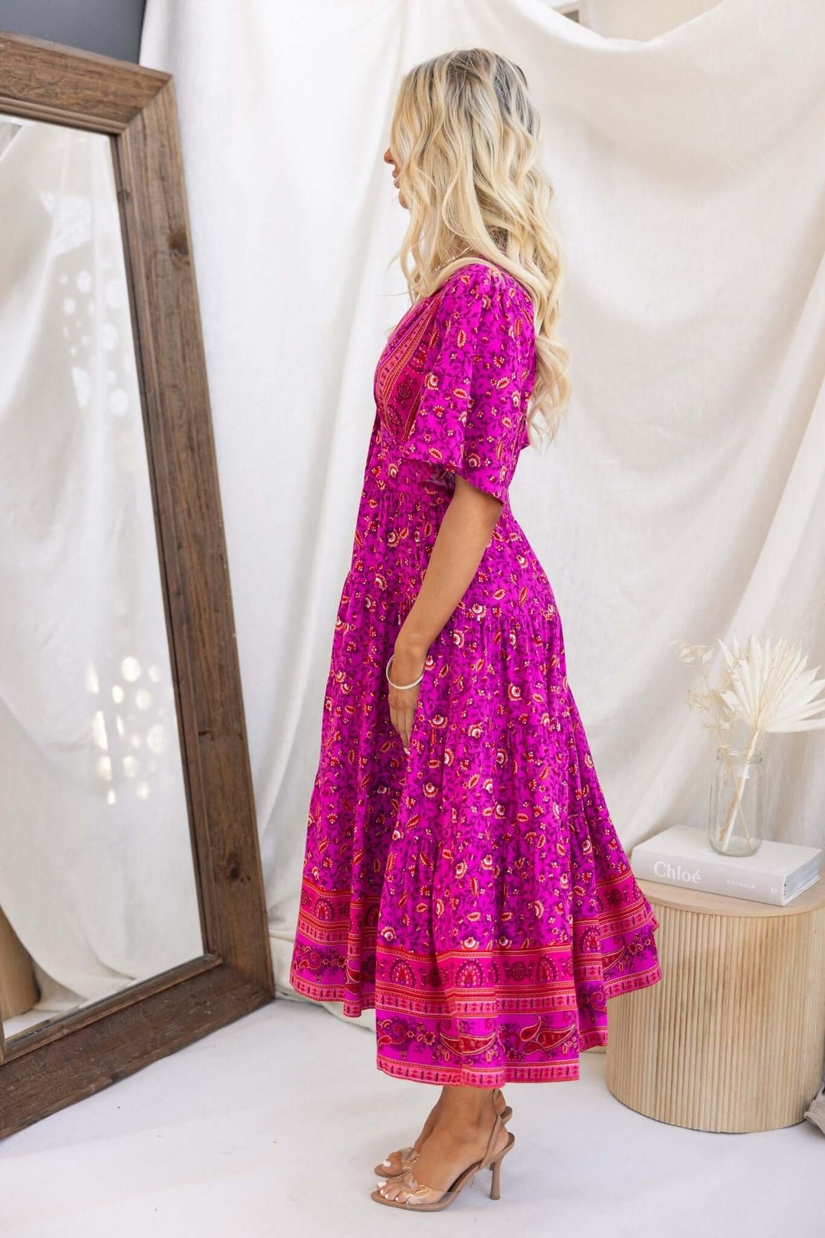 Side view of a model wearing a bright pink Hope filled Midi Dress with floral patterns and a flowing skirt.