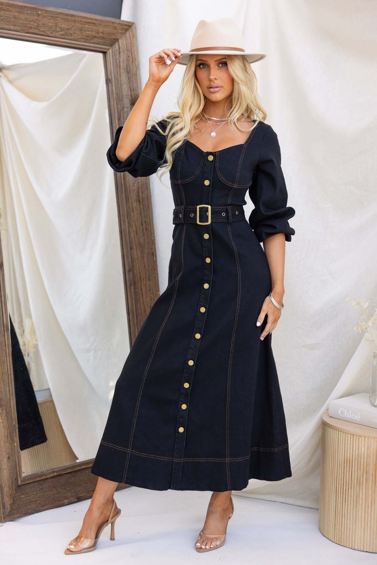 Black denim maxi dress with faux button-up front, elastic sleeves, and removable belt on model in stylish hat.