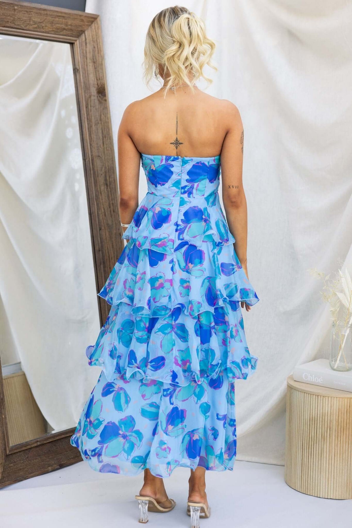 Back view of a Terrace Maxi Dress in blue floral print with layered ruffles, shown on a model.